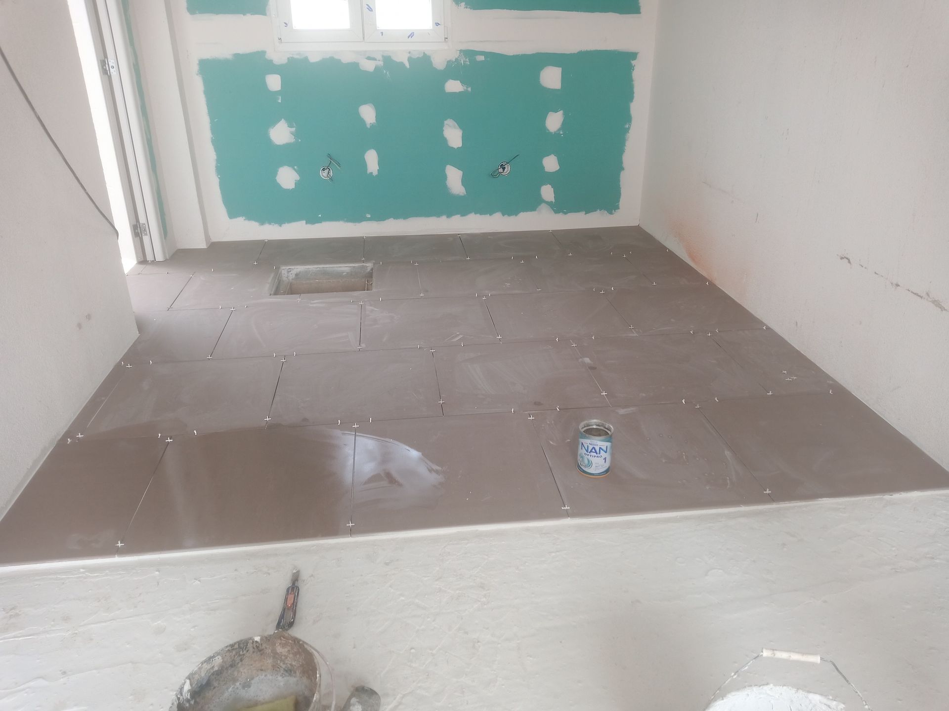 Quarto em construção: piso de azulejos marrons, paredes de gesso acartonado verde.