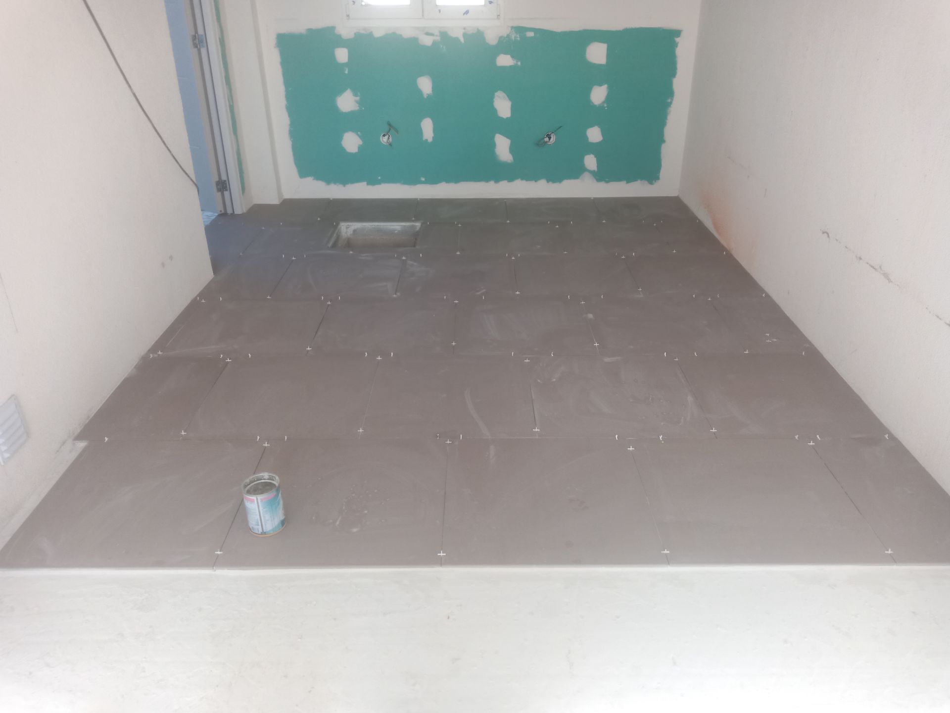 Quarto em construção com piso cinza e parede verde-azulada.