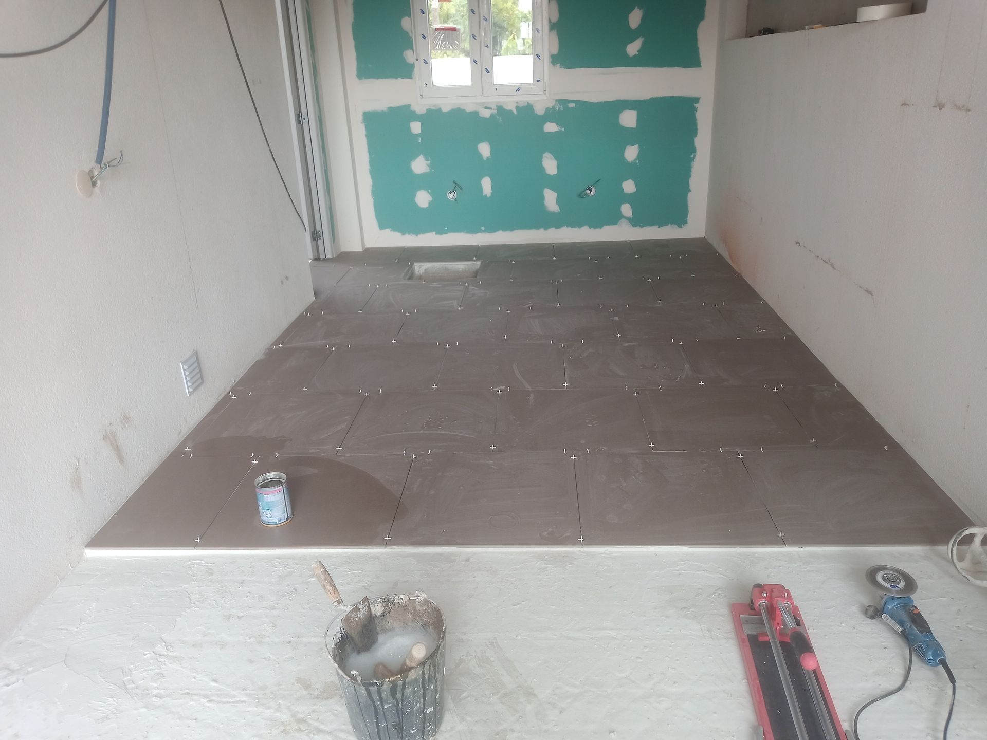 Quarto em construção com instalação de ladrilhos cinza no piso. Paredes de gesso acartonado.