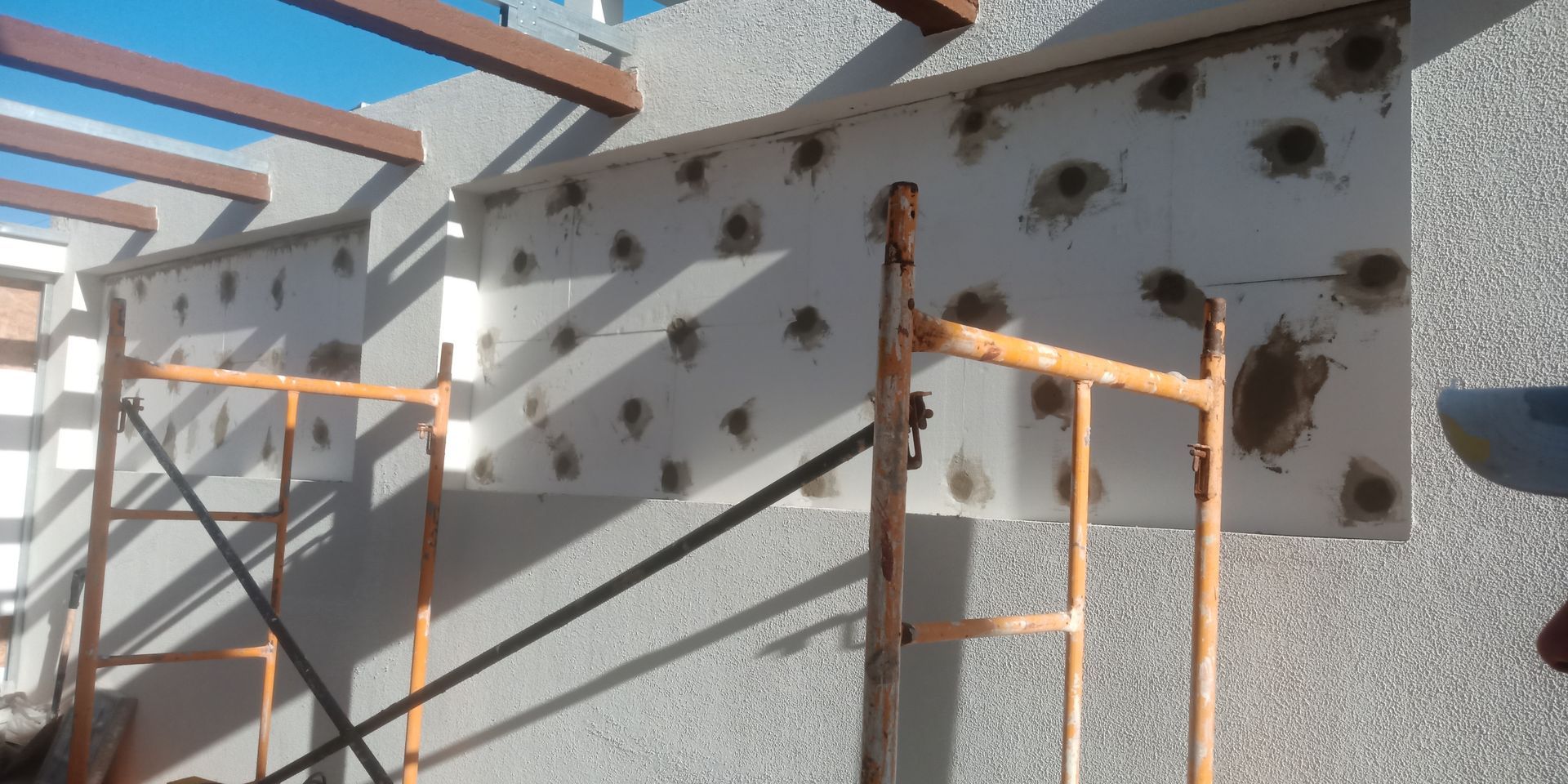 Canteiro de obras: Placa de isolamento de espuma branca fixada em parede de estuque, com andaimes.