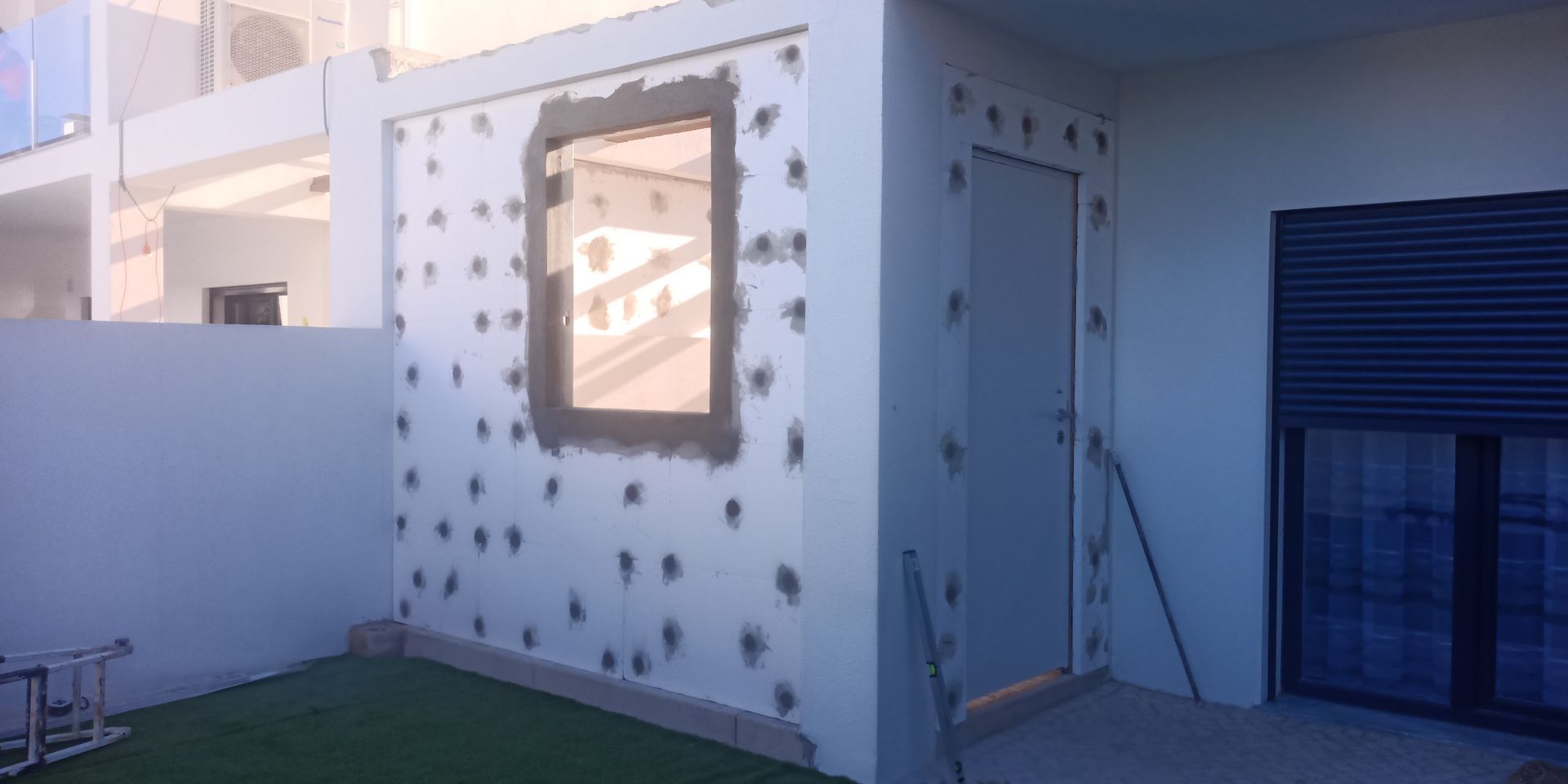Parede externa com janela e porta, pontilhada com fixadores, em construção.