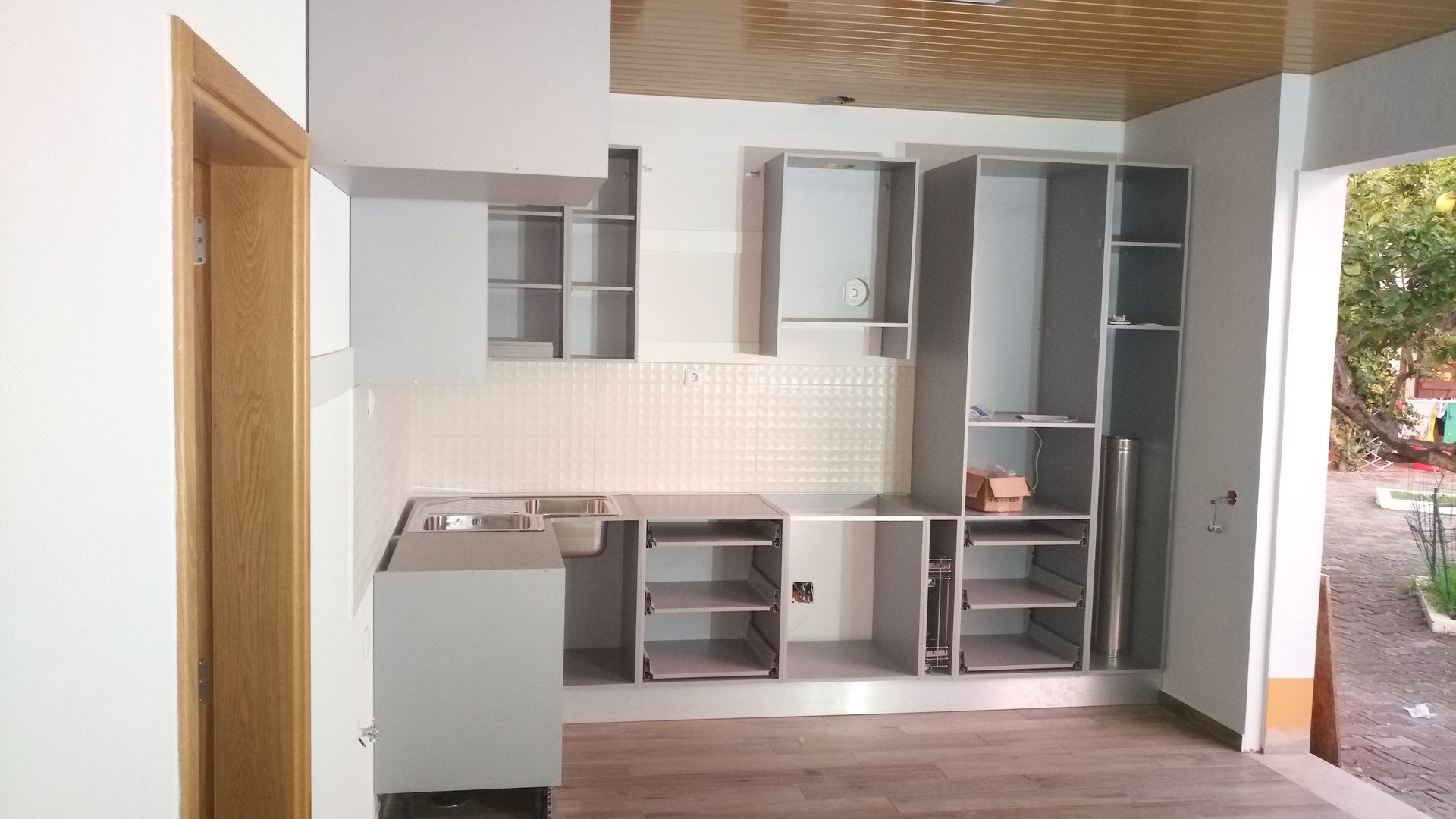 Armários de cozinha em um cômodo com painel perfurado na parede, coifa, pia e piso de madeira.