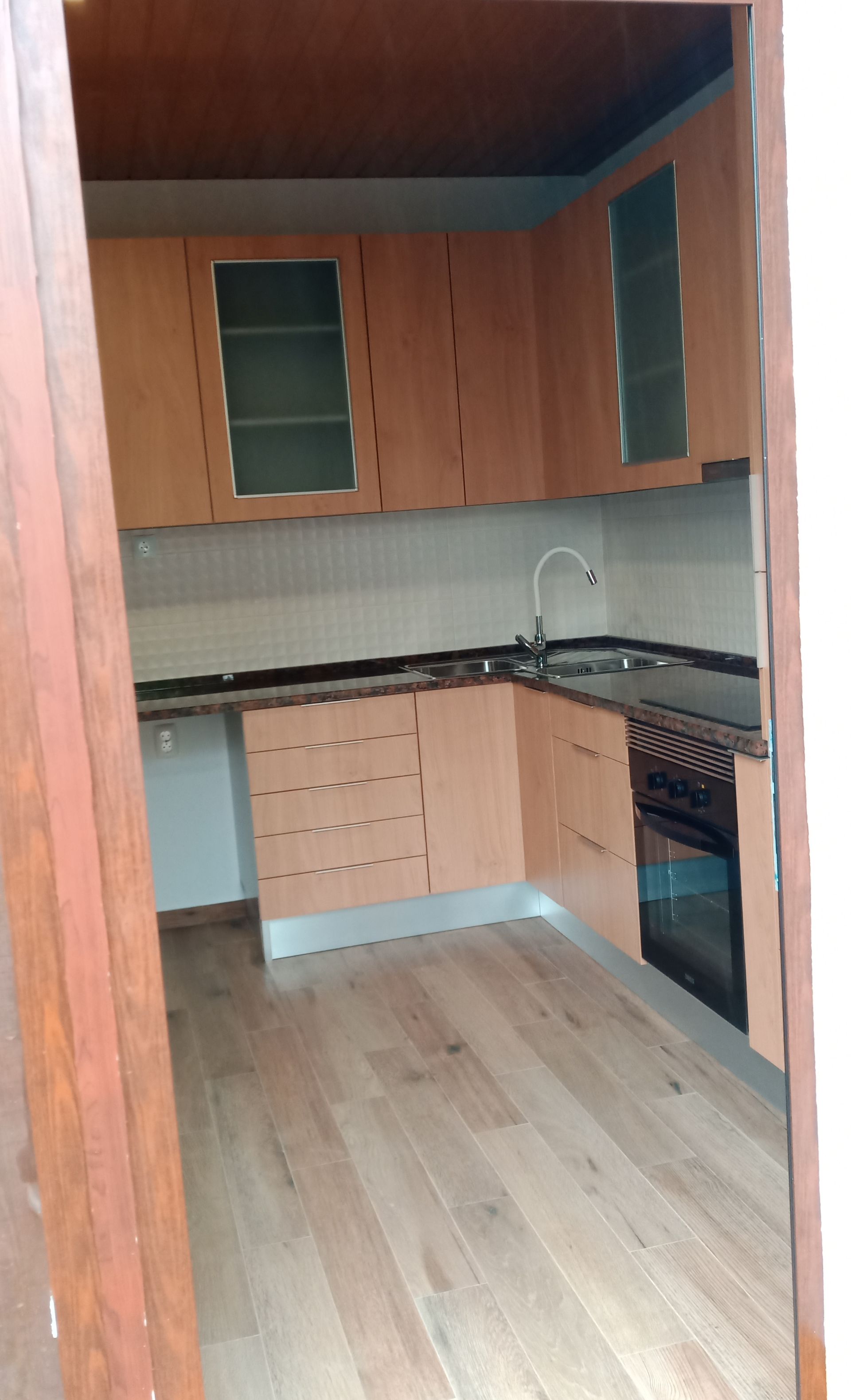 Cozinha pequena com armários de madeira, bancadas escuras e forno; piso de madeira clara.