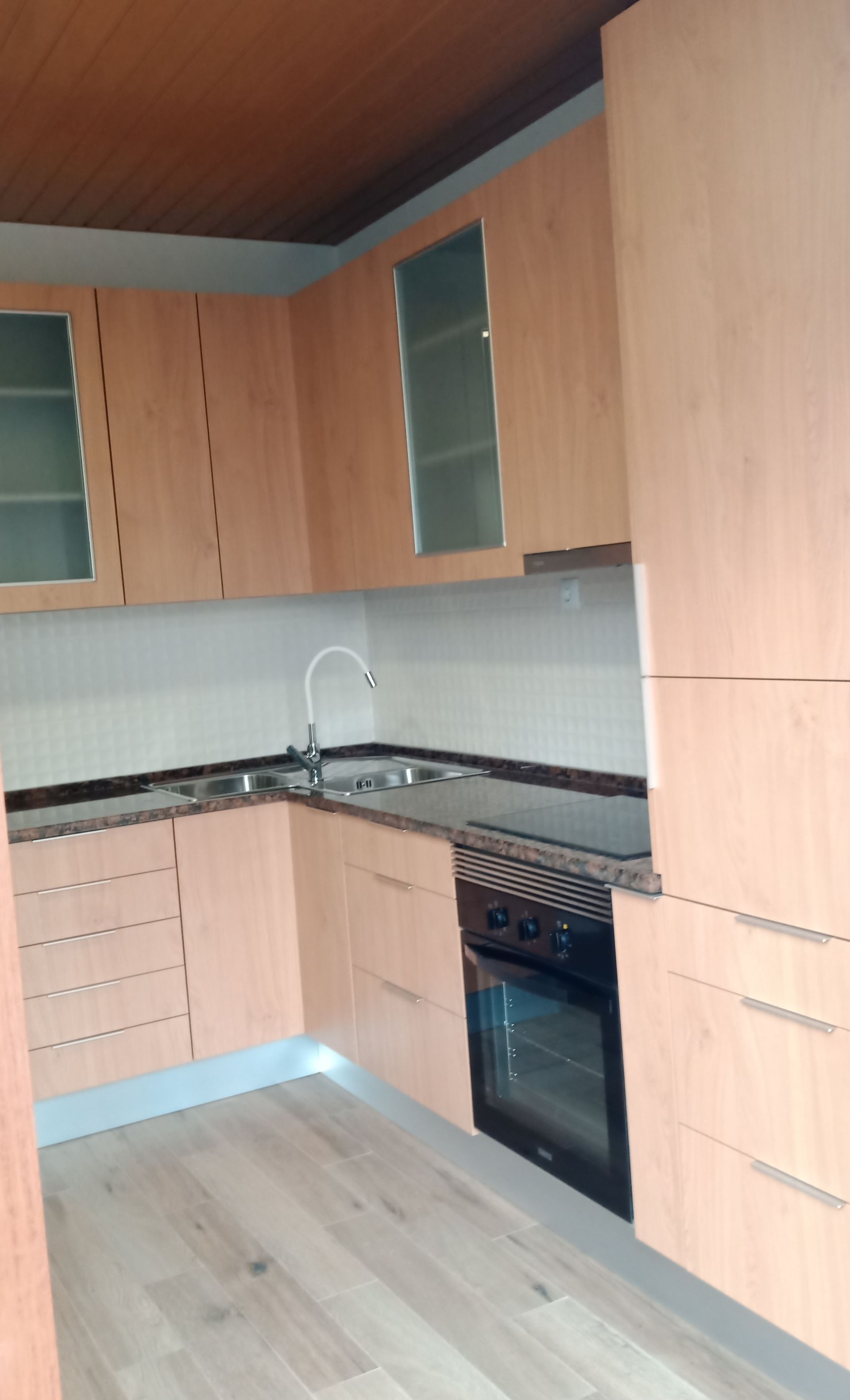 Armários de cozinha bege com bancadas pretas, torneira prateada e forno embutido.