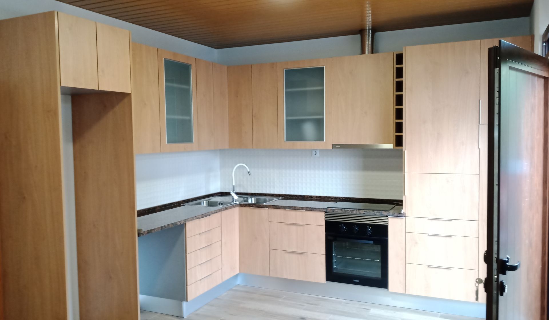 Armários de cozinha bege com bancadas, pia, forno e geladeira.