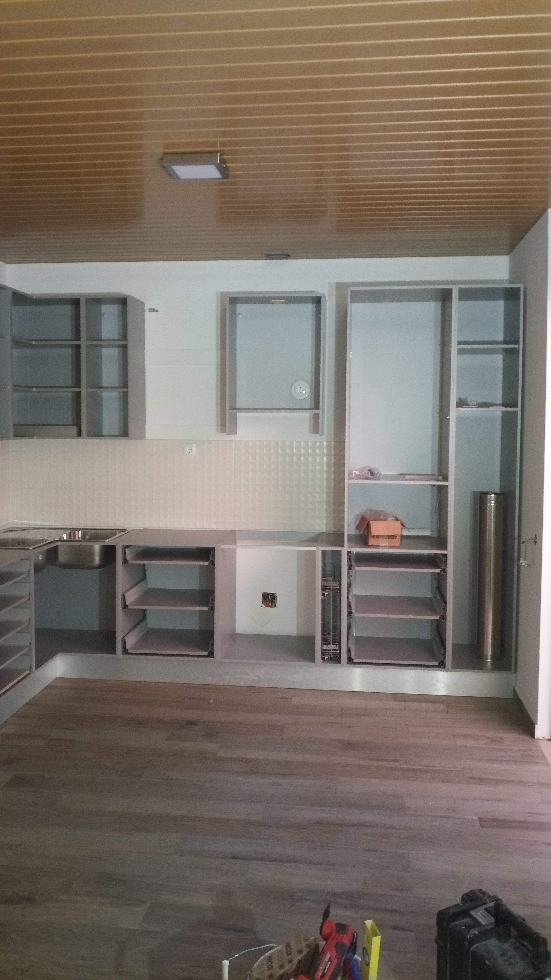 Cozinha em construção com armários inacabados, backsplash e piso de madeira.
