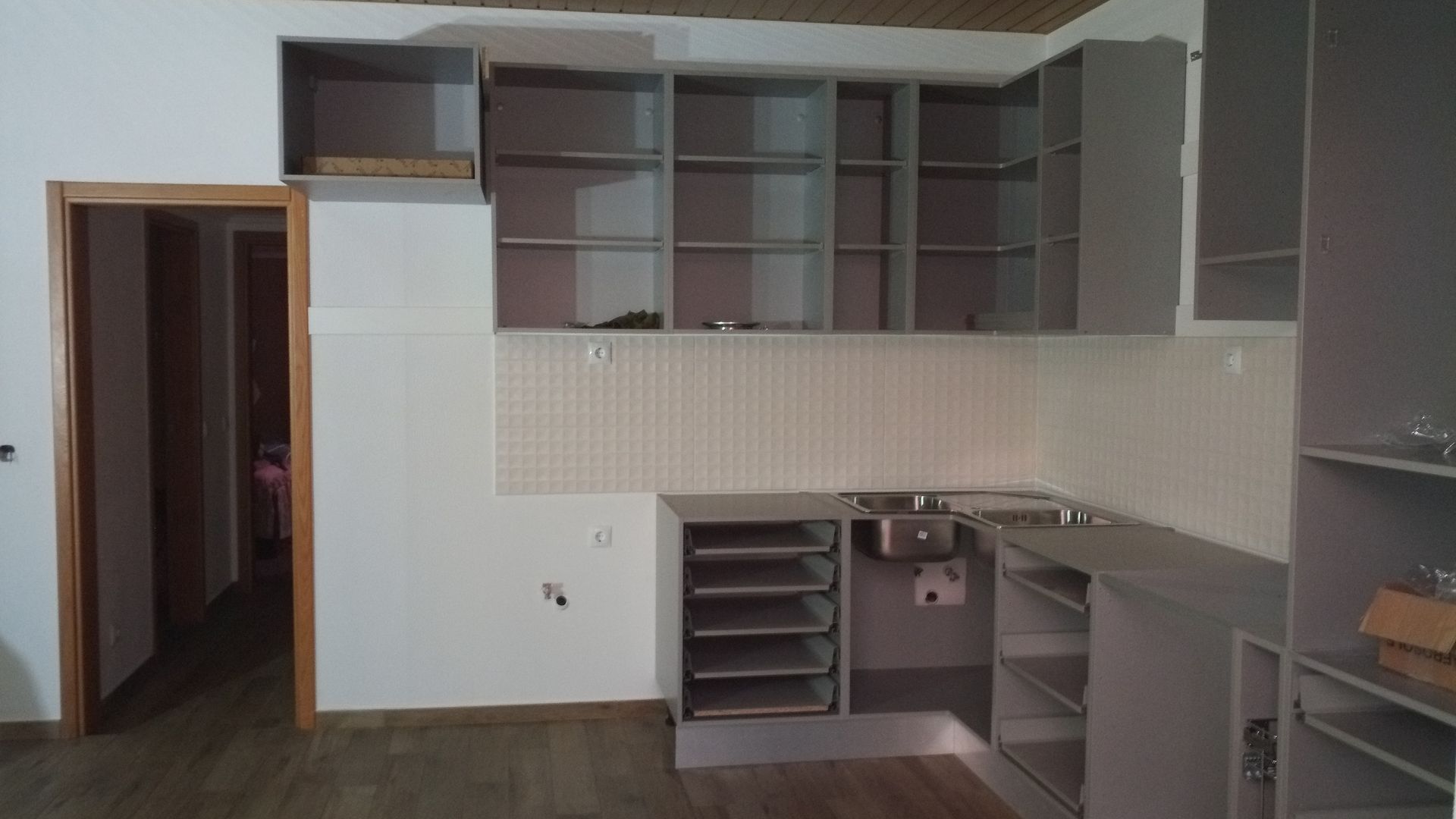 Cozinha com armários e prateleiras cinza, uma pia e uma porta.