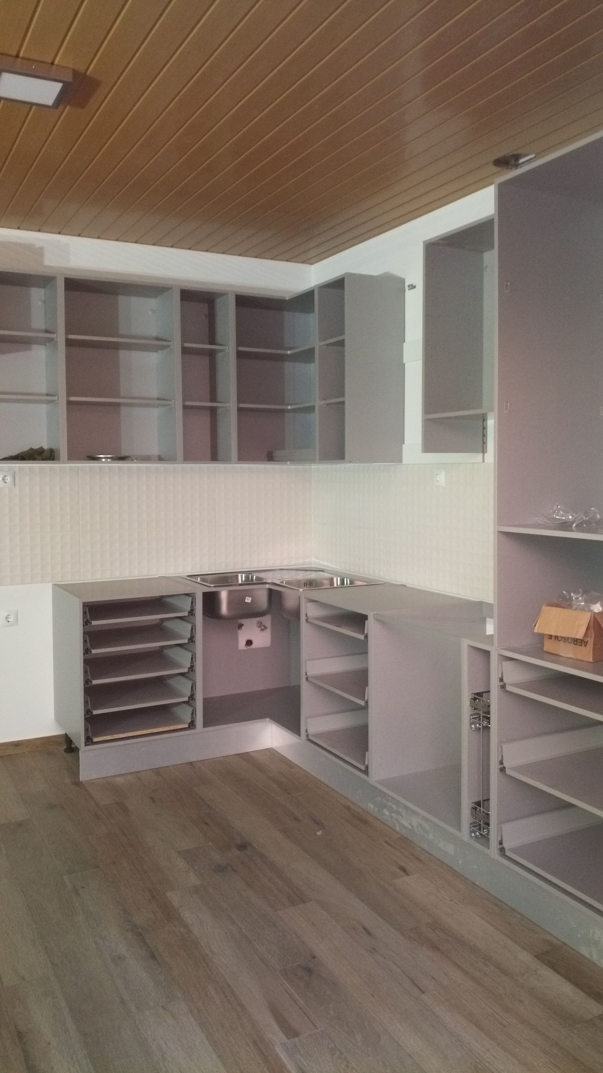Cozinha inacabada com armários cinza, prateleiras prateadas e piso de madeira.