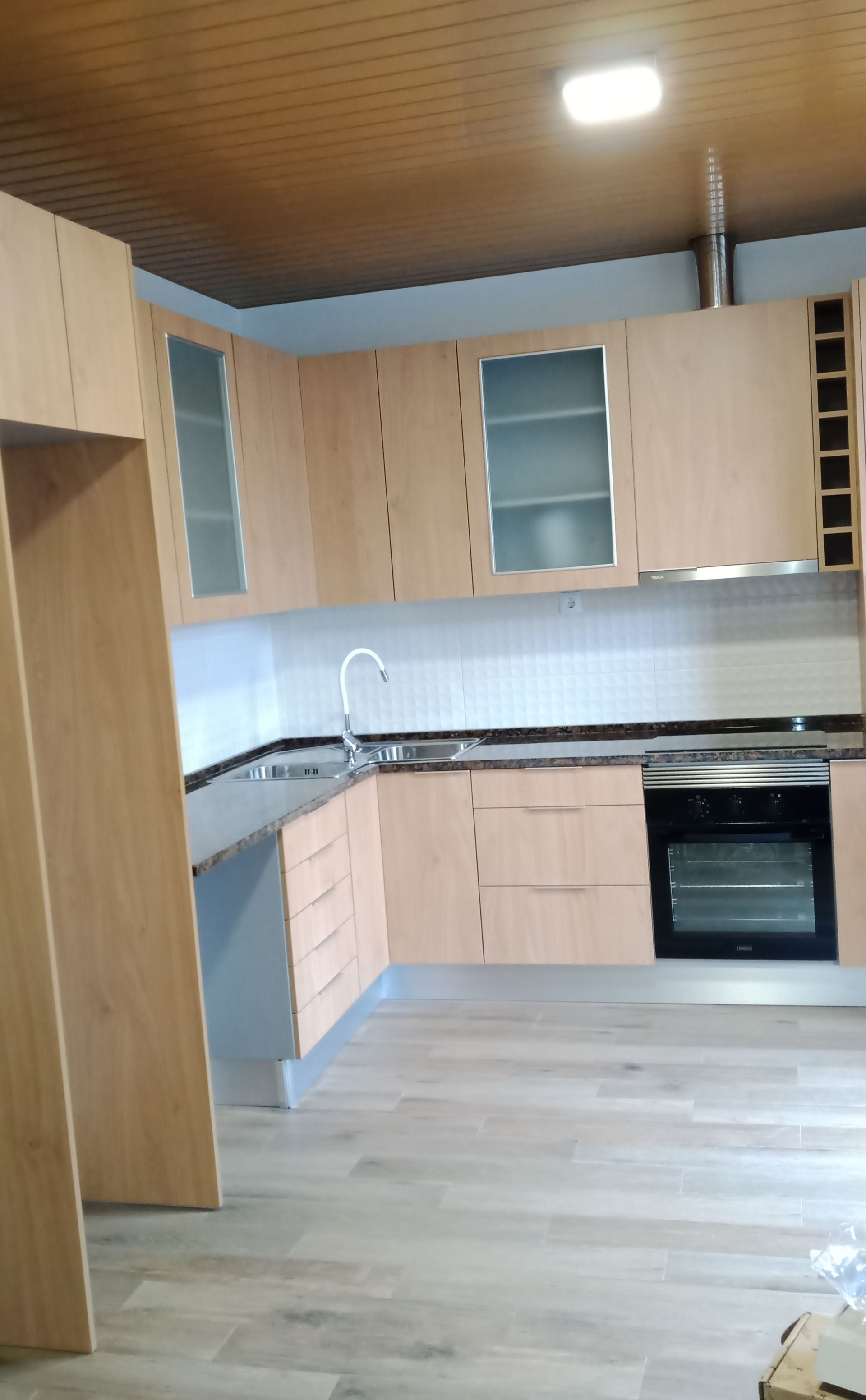 Cozinha moderna com armários de madeira clara, bancadas cinza e eletrodomésticos de aço inoxidável.