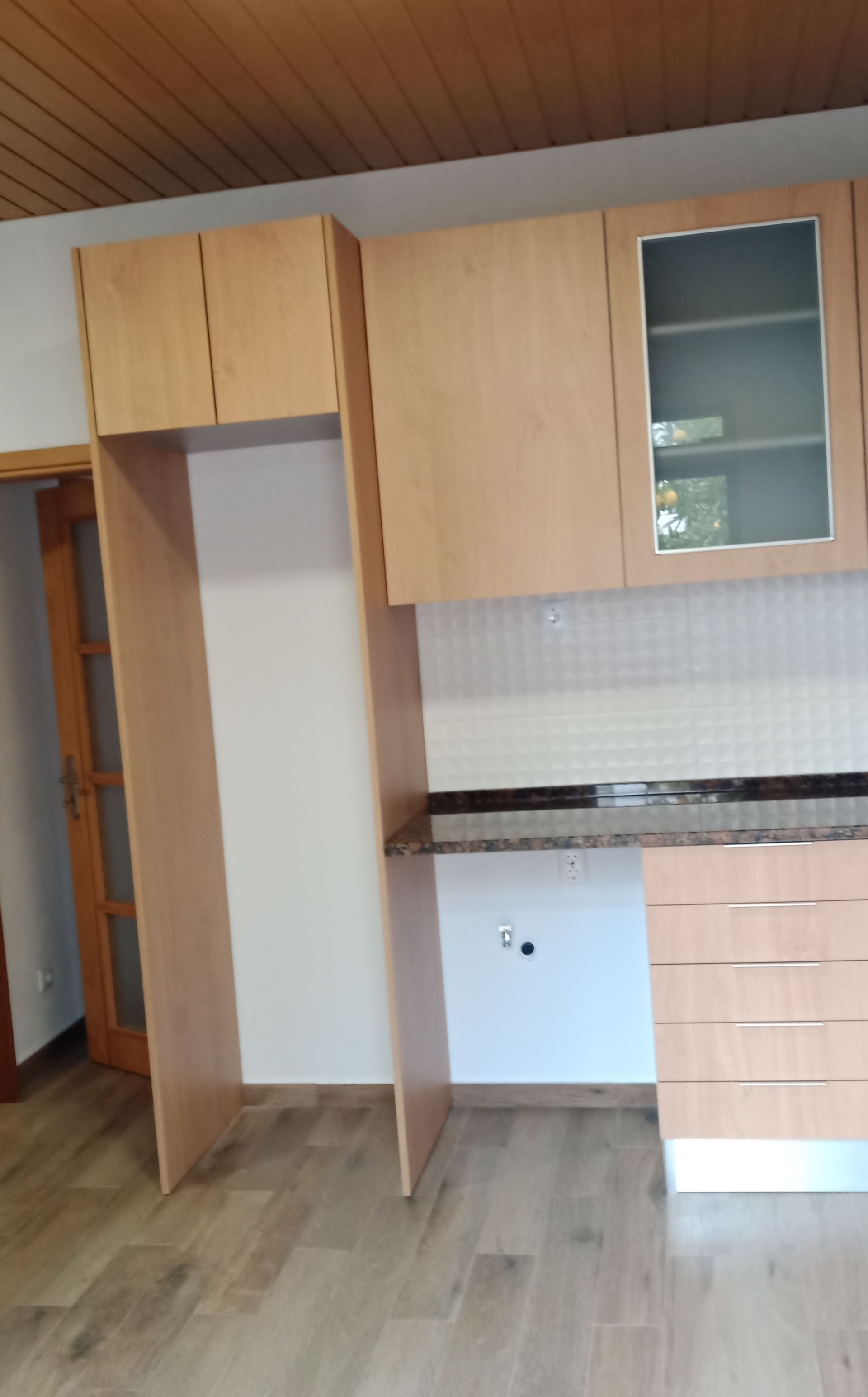 Armários de cozinha com acabamento em madeira clara, com espaço para geladeira.