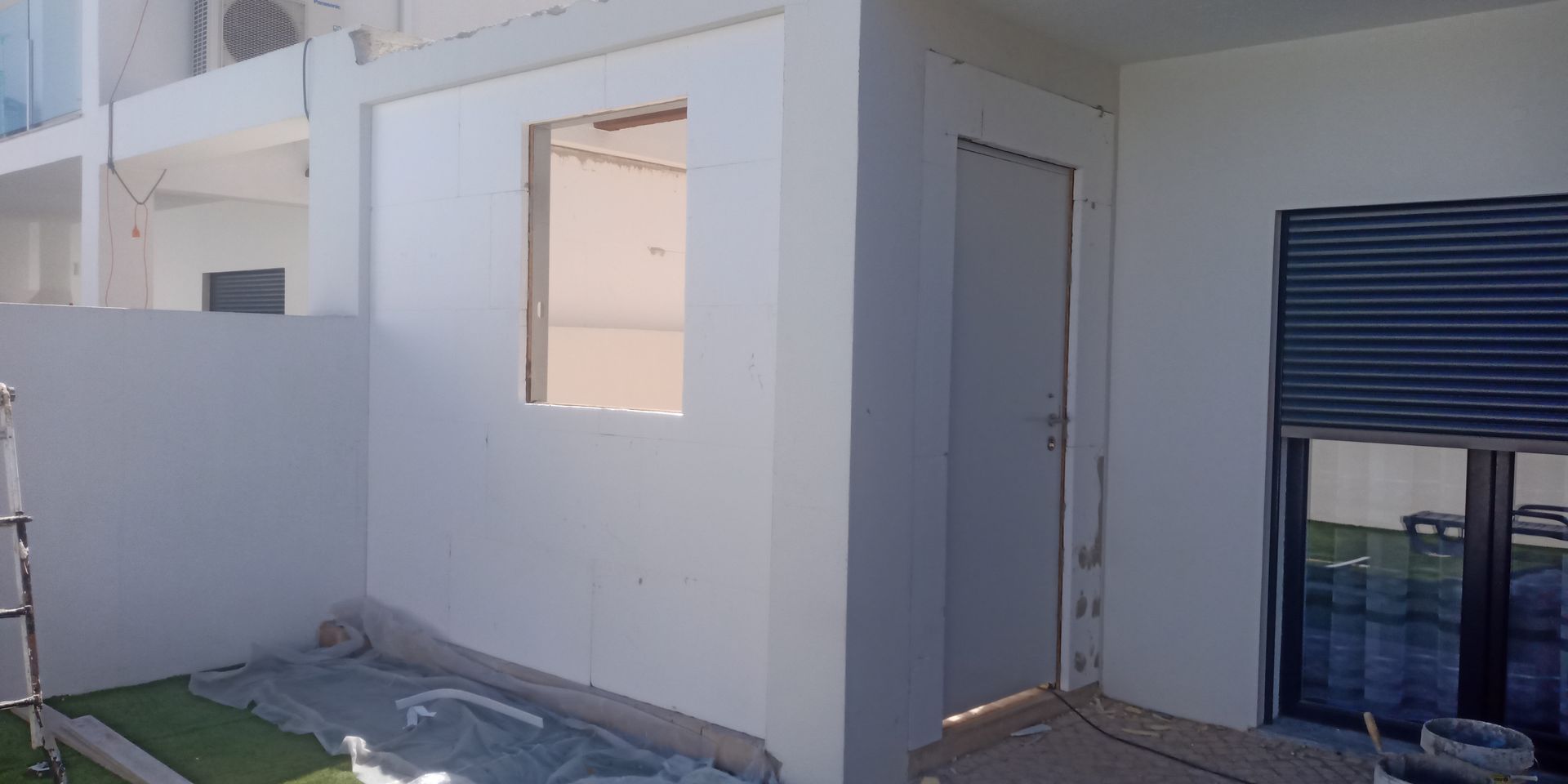 Exterior de um edifício com janela, porta e persianas, recém-pintado de branco.