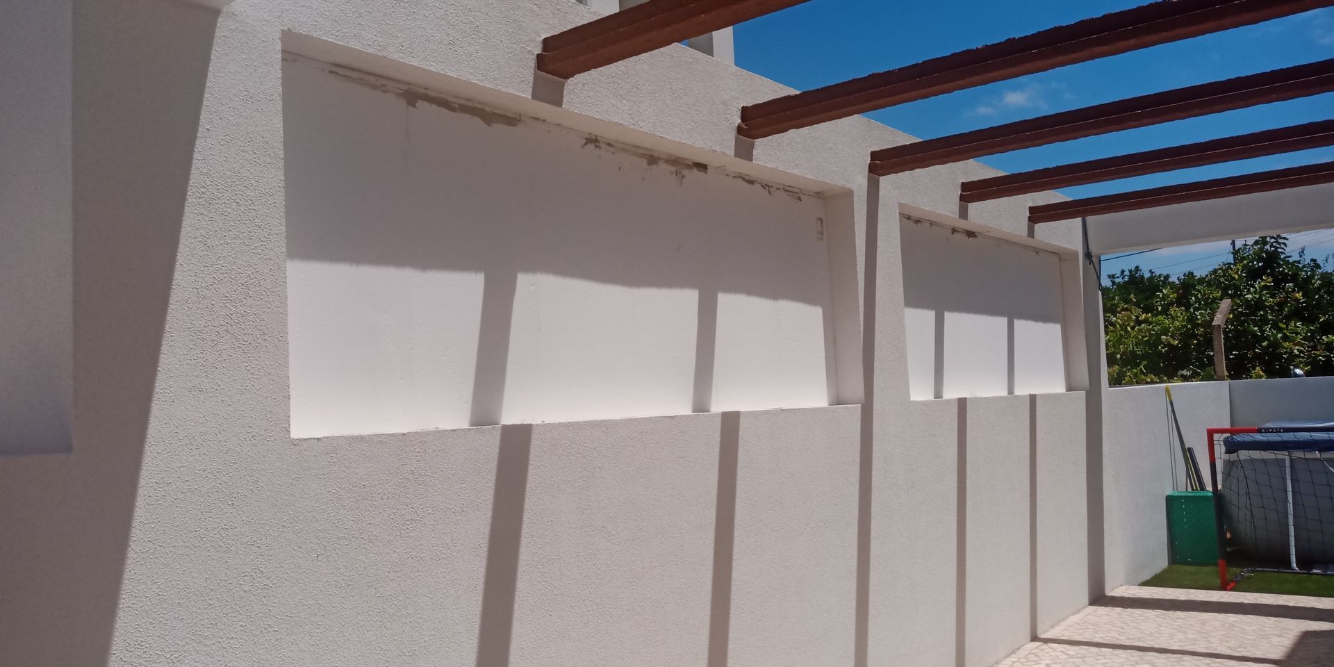 Exterior de um edifício com paredes brancas, vigas de madeira e persianas brancas. O céu é visível.