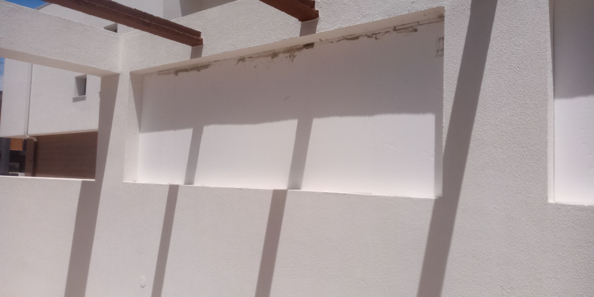 Foto exterior de um edifício de estuque branco com aberturas retangulares que projetam sombras na parede.