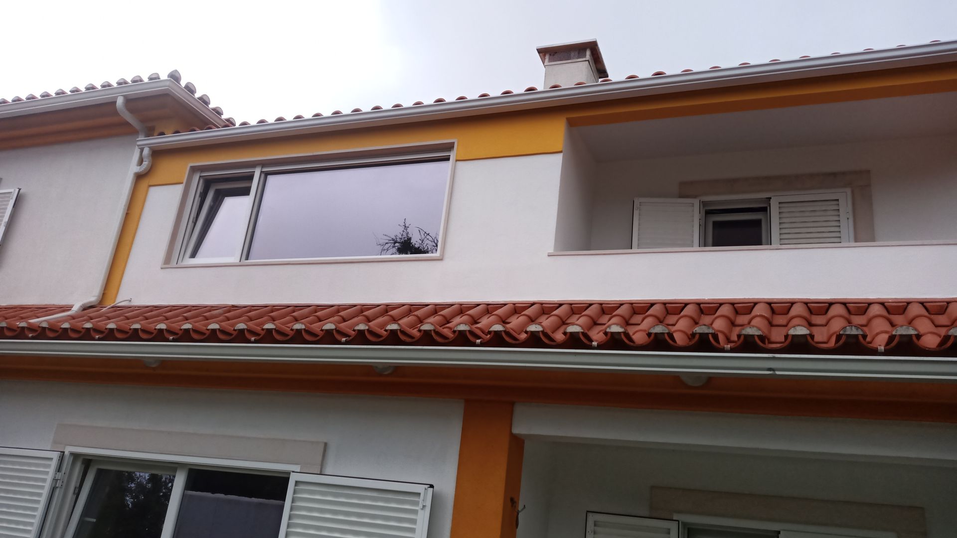 Prédio branco de dois andares com detalhes em laranja e telhado de telha vermelha; janelas visíveis.