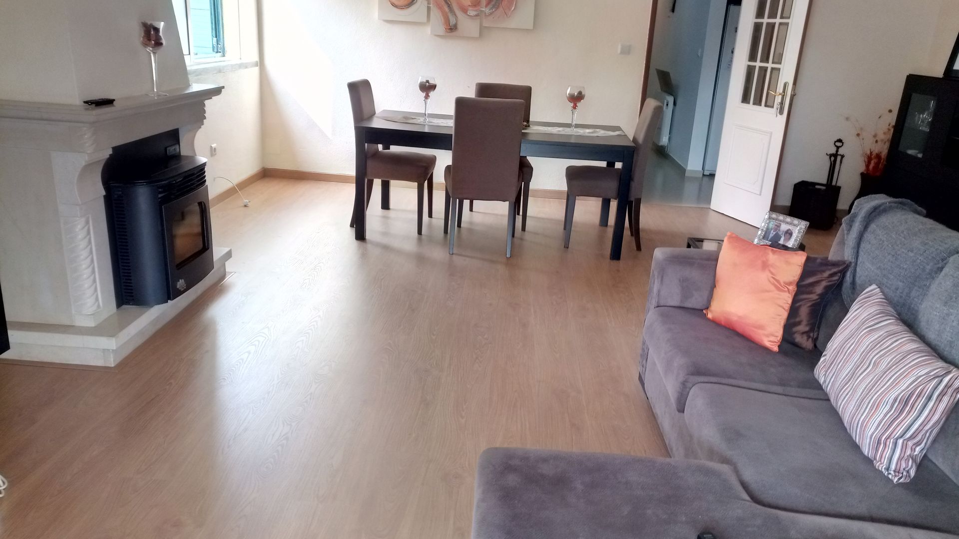 Sala de estar com lareira, mesa de jantar e sofá cinza; piso de madeira.