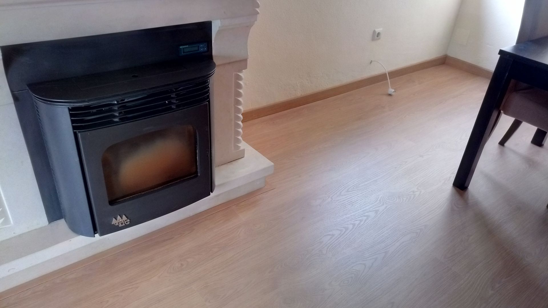 Lareira preta embutida em uma moldura branca, sobre um piso de madeira marrom-claro ao lado de uma mesa.