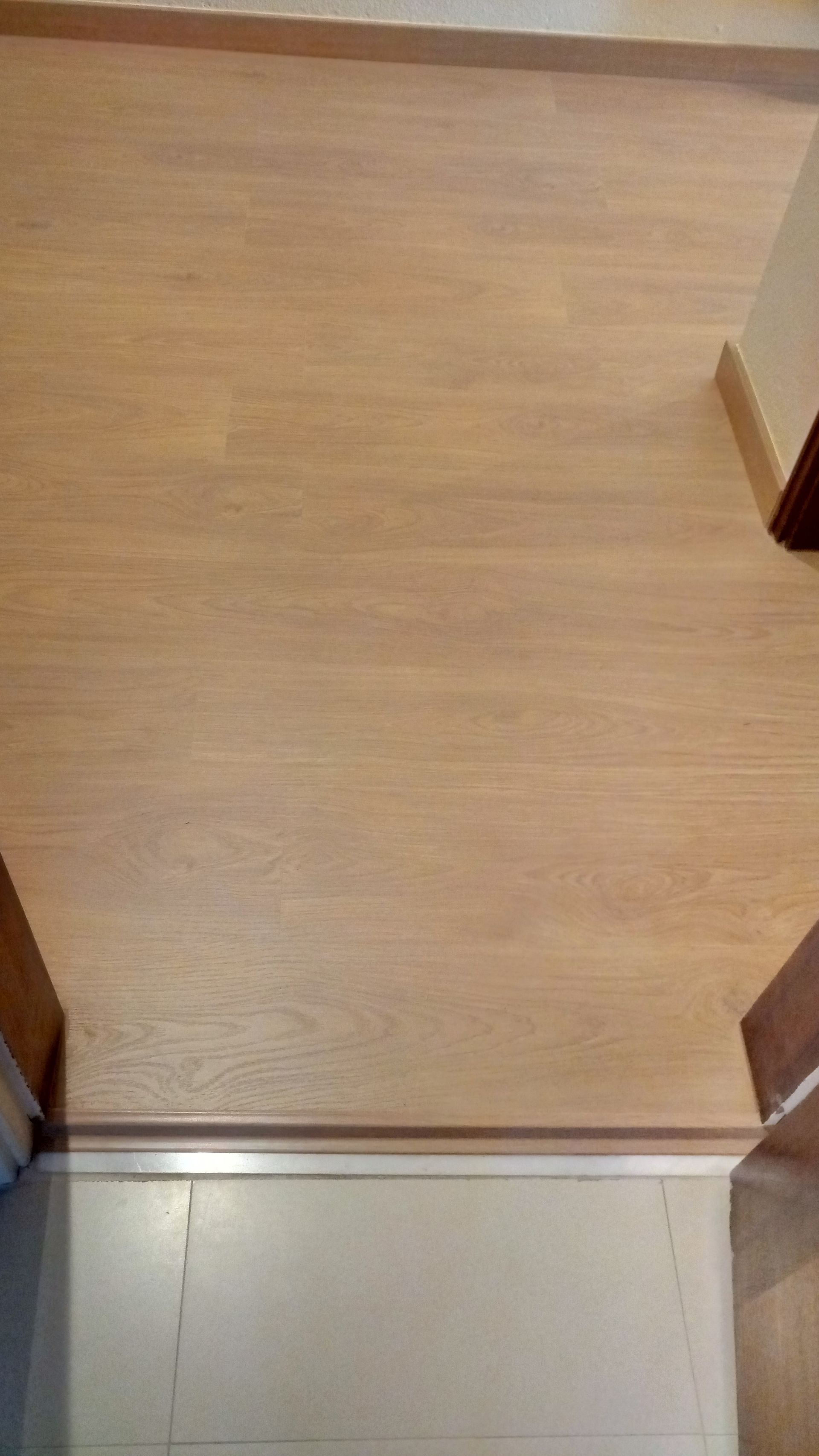 O piso de madeira marrom-claro faz a transição para um piso de azulejos cinza-claro.