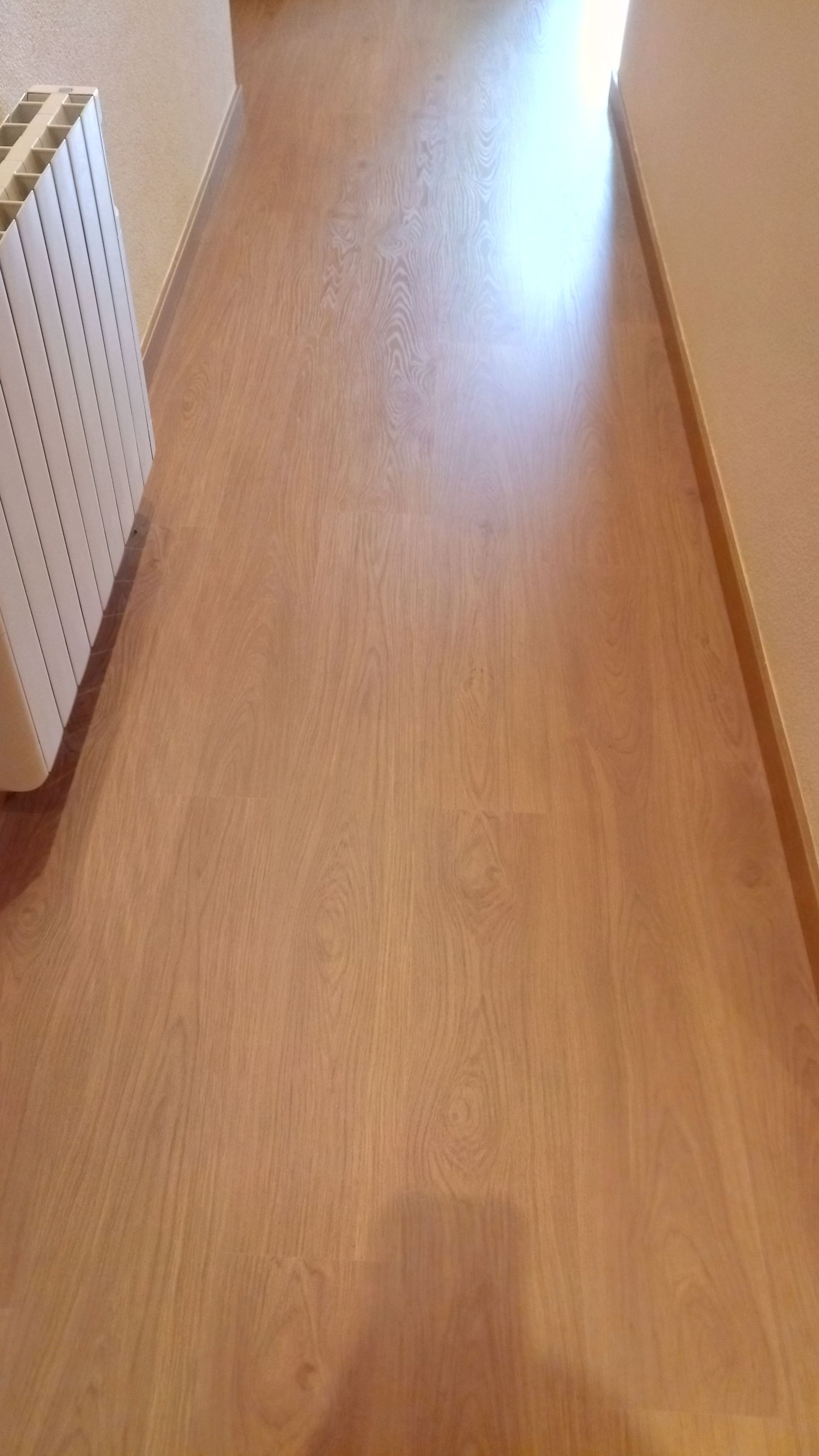 Piso de madeira castanho-claro com um painel perfurado branco e uma tábua de madeira nas laterais.