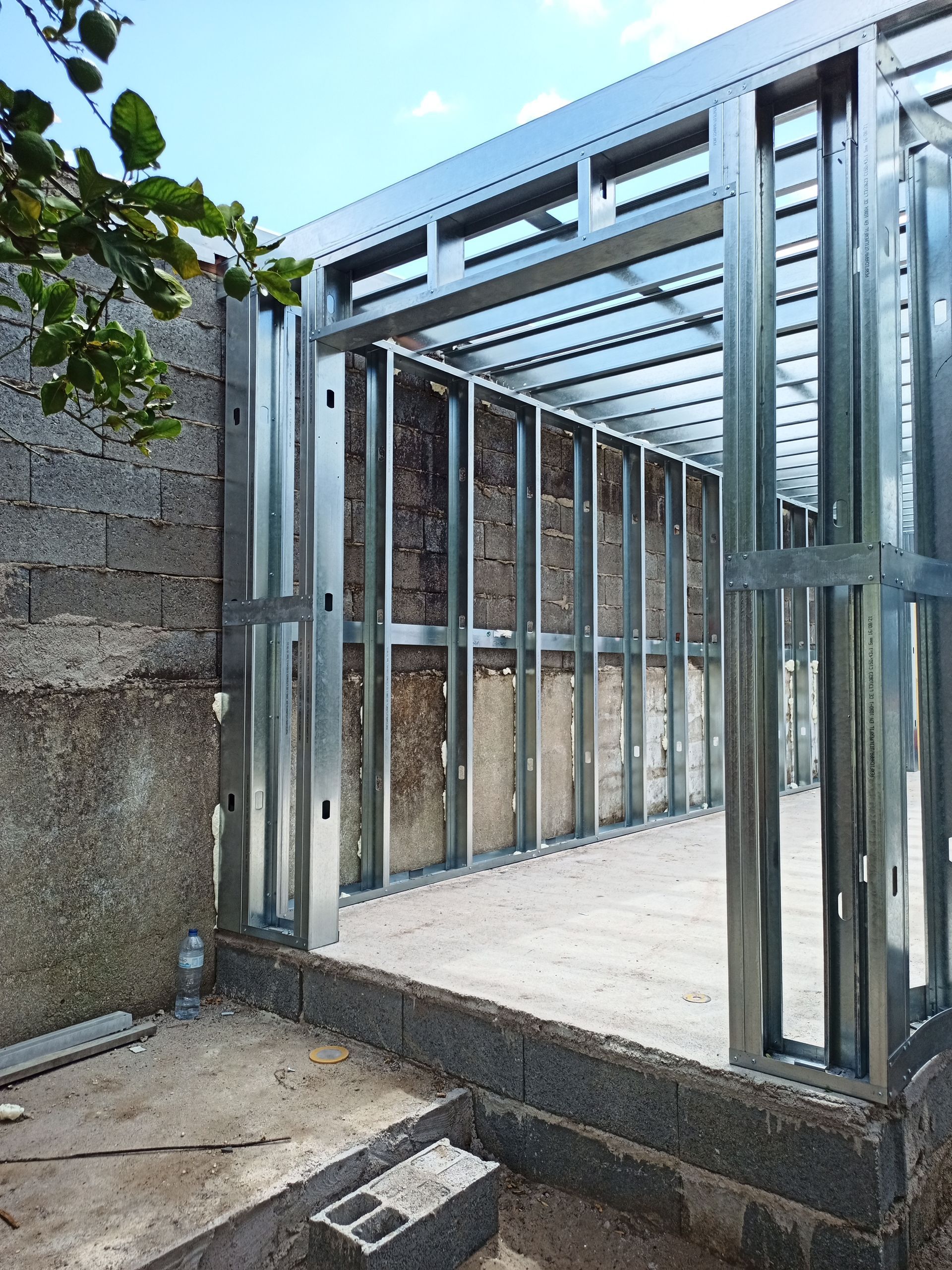 Estrutura metálica de um edifício em construção, fixada a uma parede de tijolos.