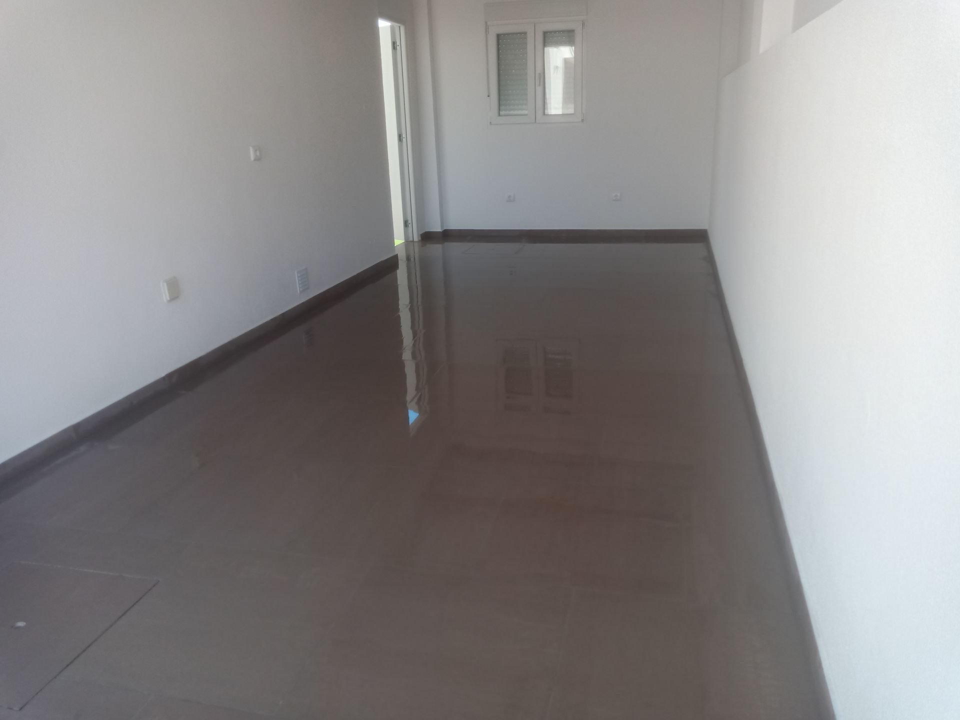 Quarto vazio com piso brilhante cinza-escuro, paredes brancas e uma janela.