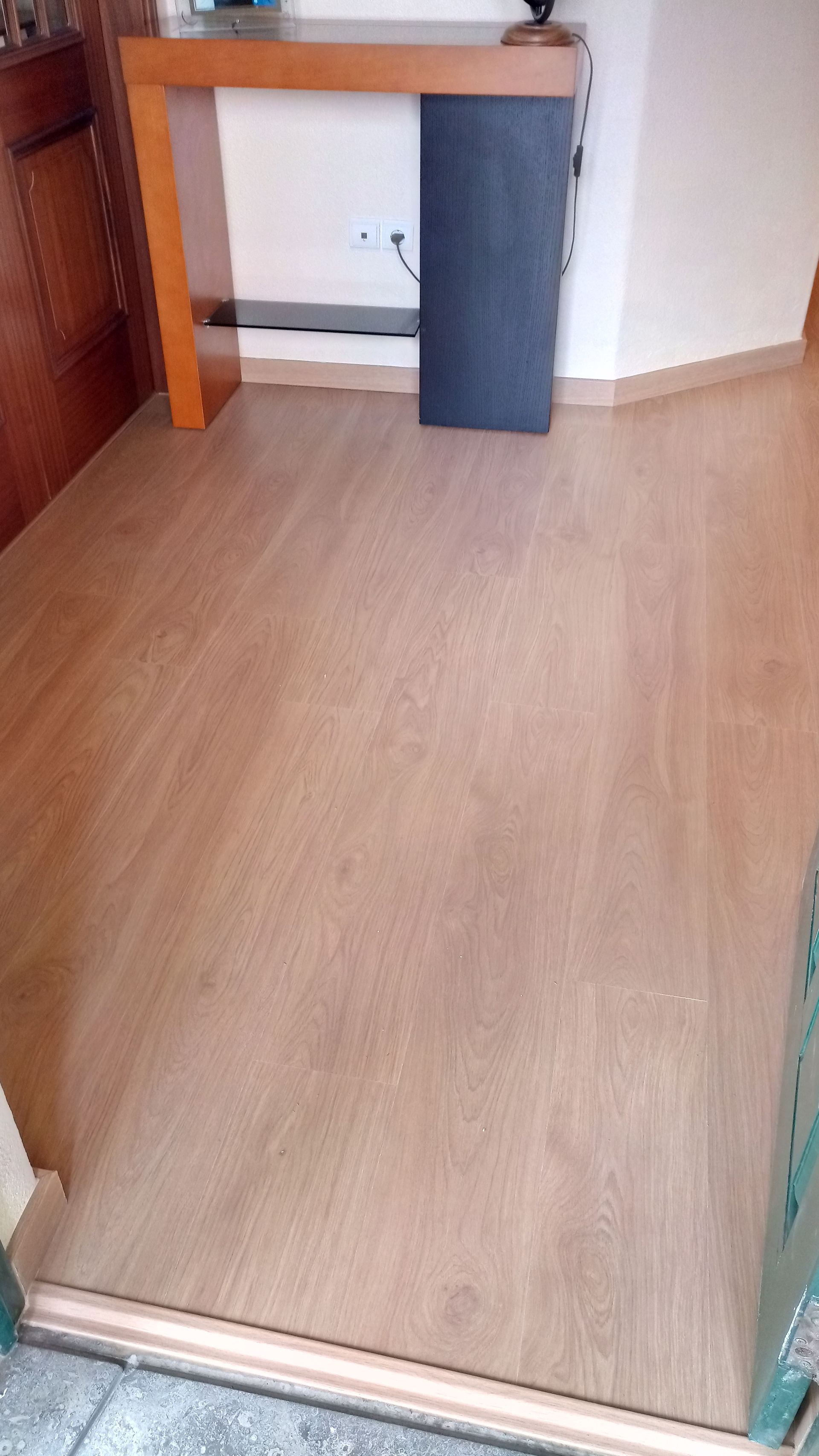 Piso de madeira em um corredor com uma mesa de apoio e um painel escuro.