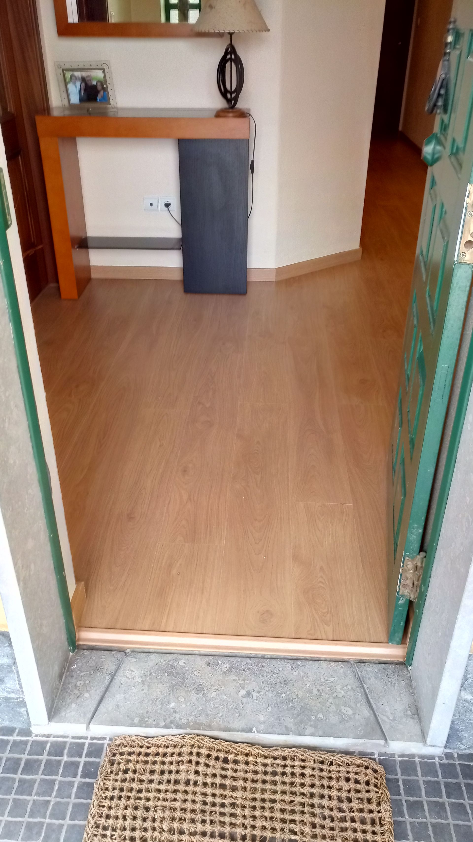 Hall de entrada com piso de madeira, capacho, mesa de apoio e porta aberta.