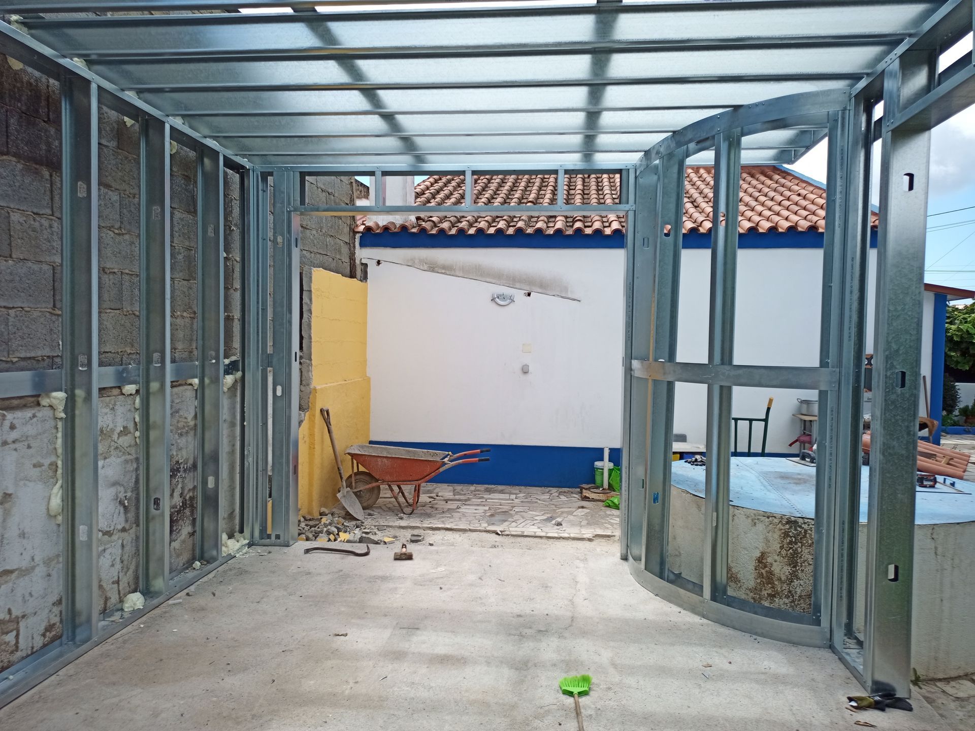 Vista interna de uma estrutura metálica com uma porta em arco que dá acesso a um pátio.