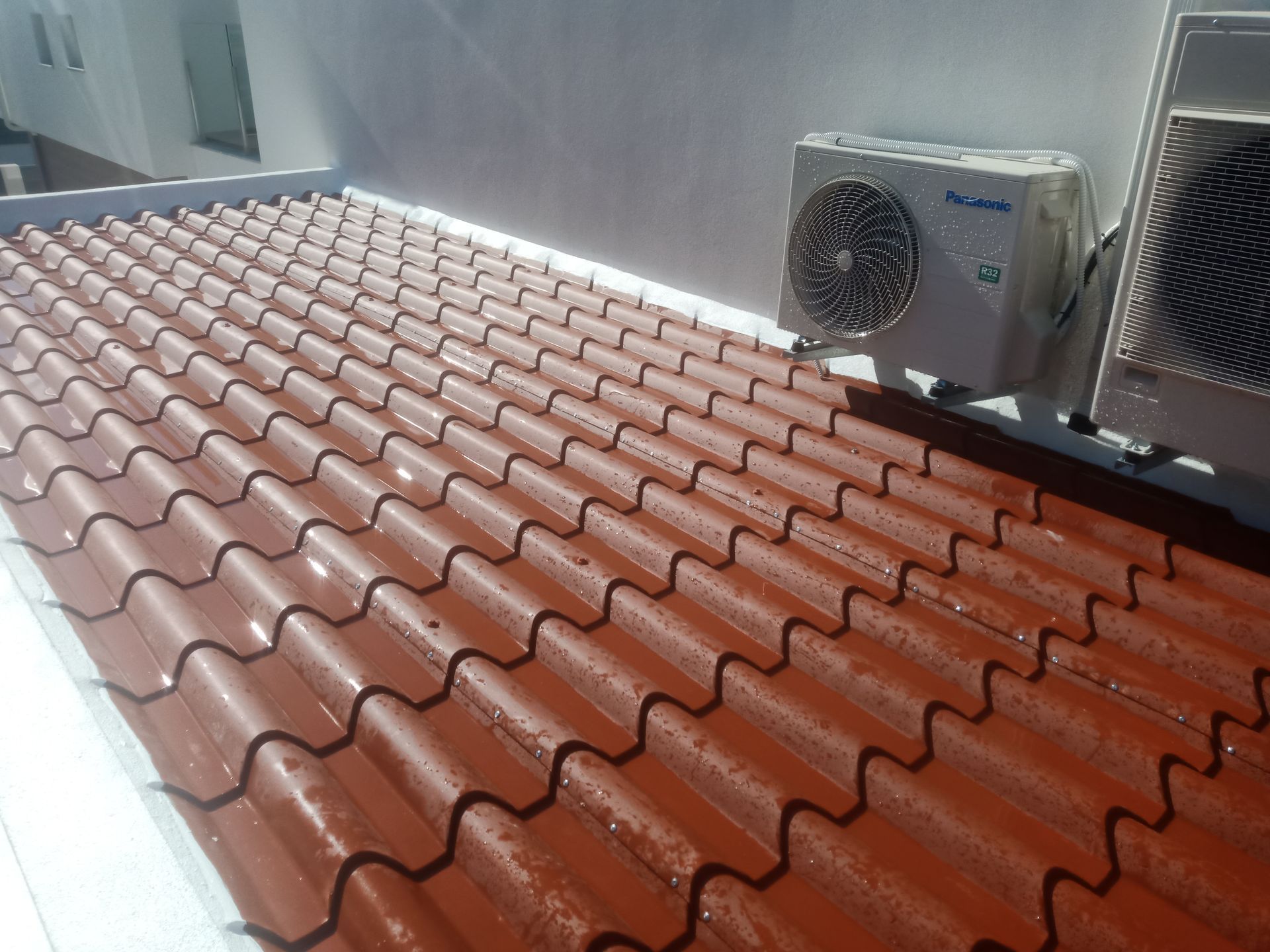 Telhado de telhas vermelhas com unidades de ar condicionado contra uma parede branca.