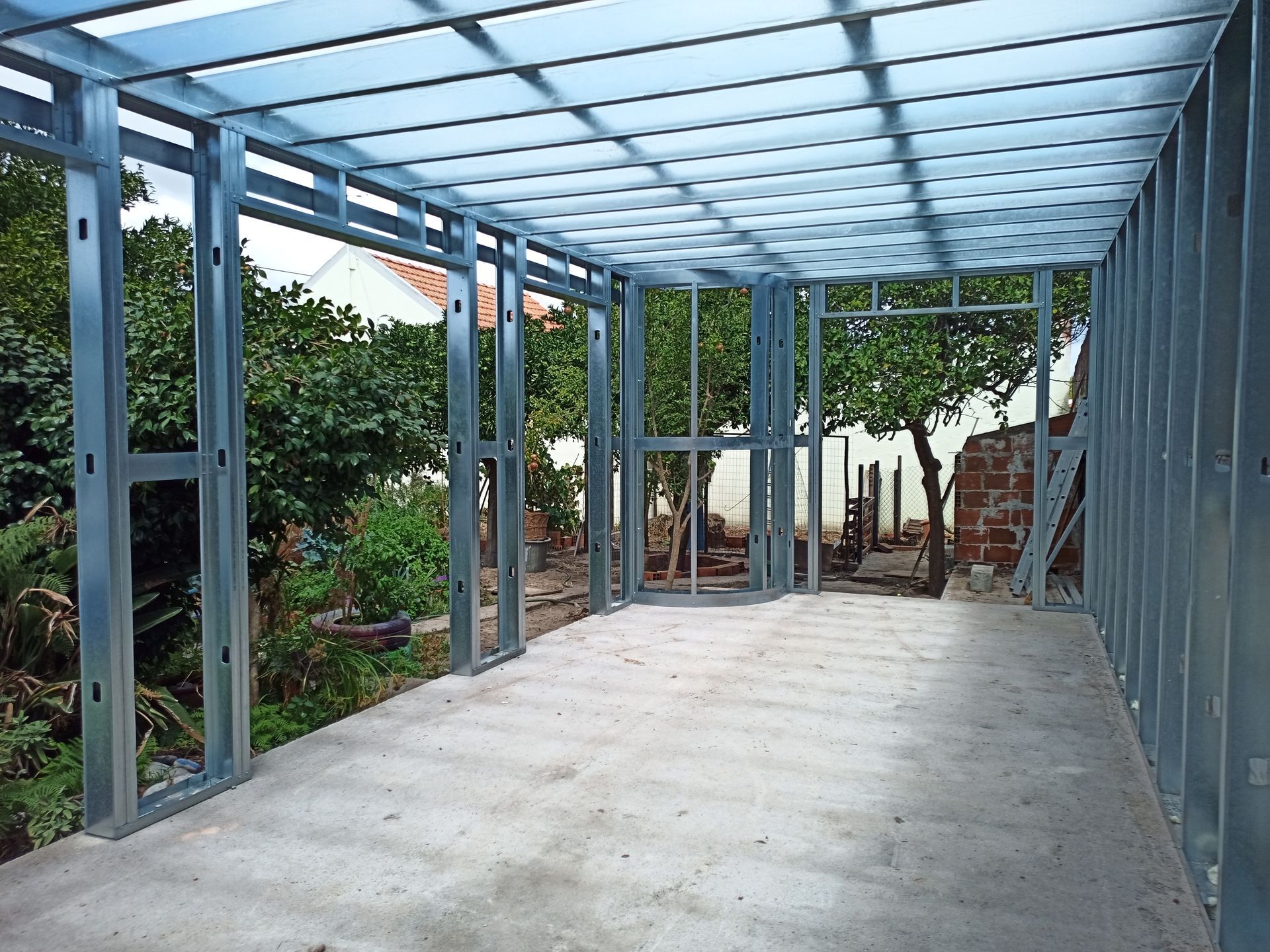 Estrutura metálica para o interior e telhado de um edifício, assentada sobre piso de concreto com vista para o quintal.