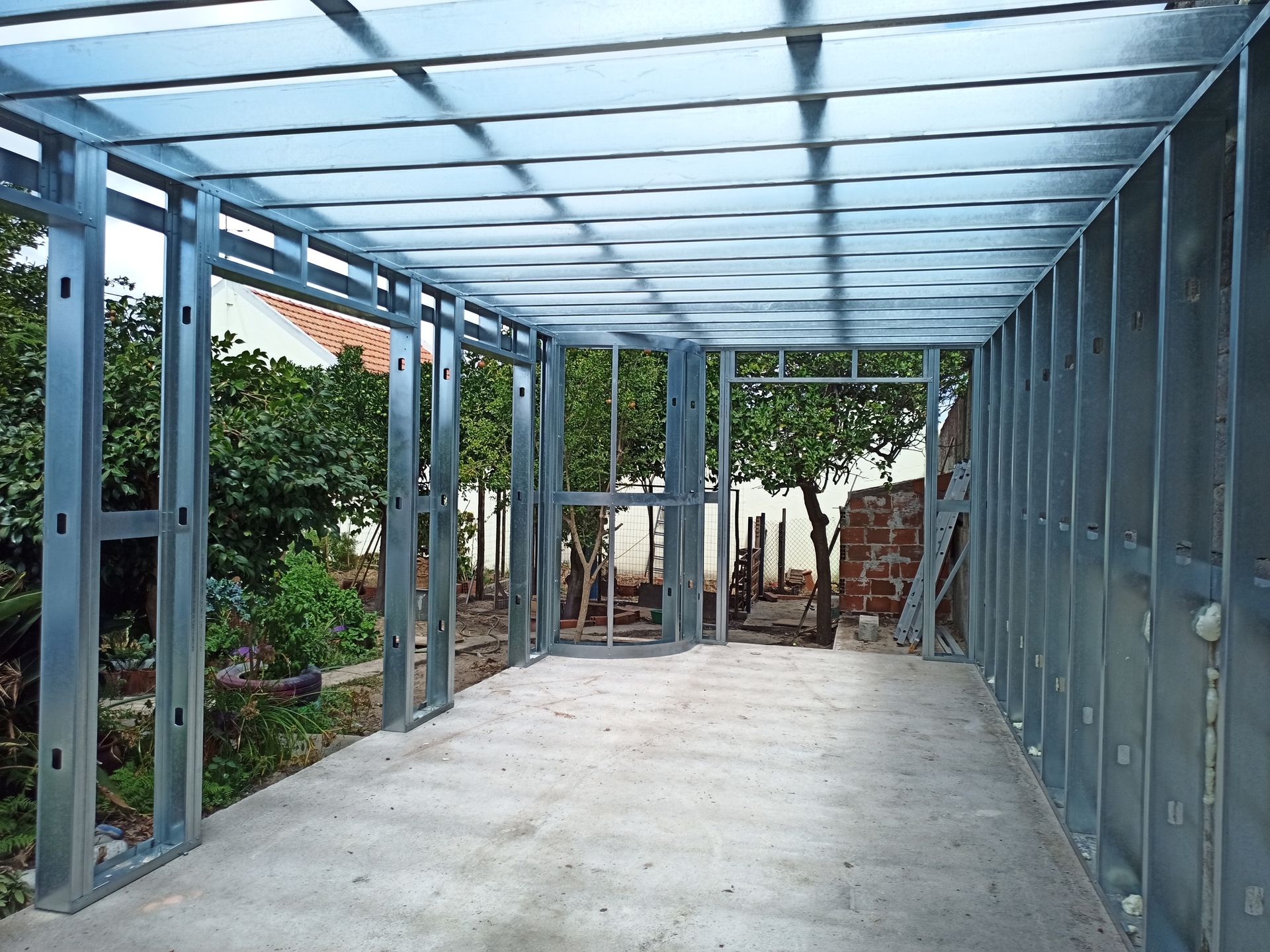 Estrutura metálica de uma sala em construção, com laterais abertas e piso de concreto.