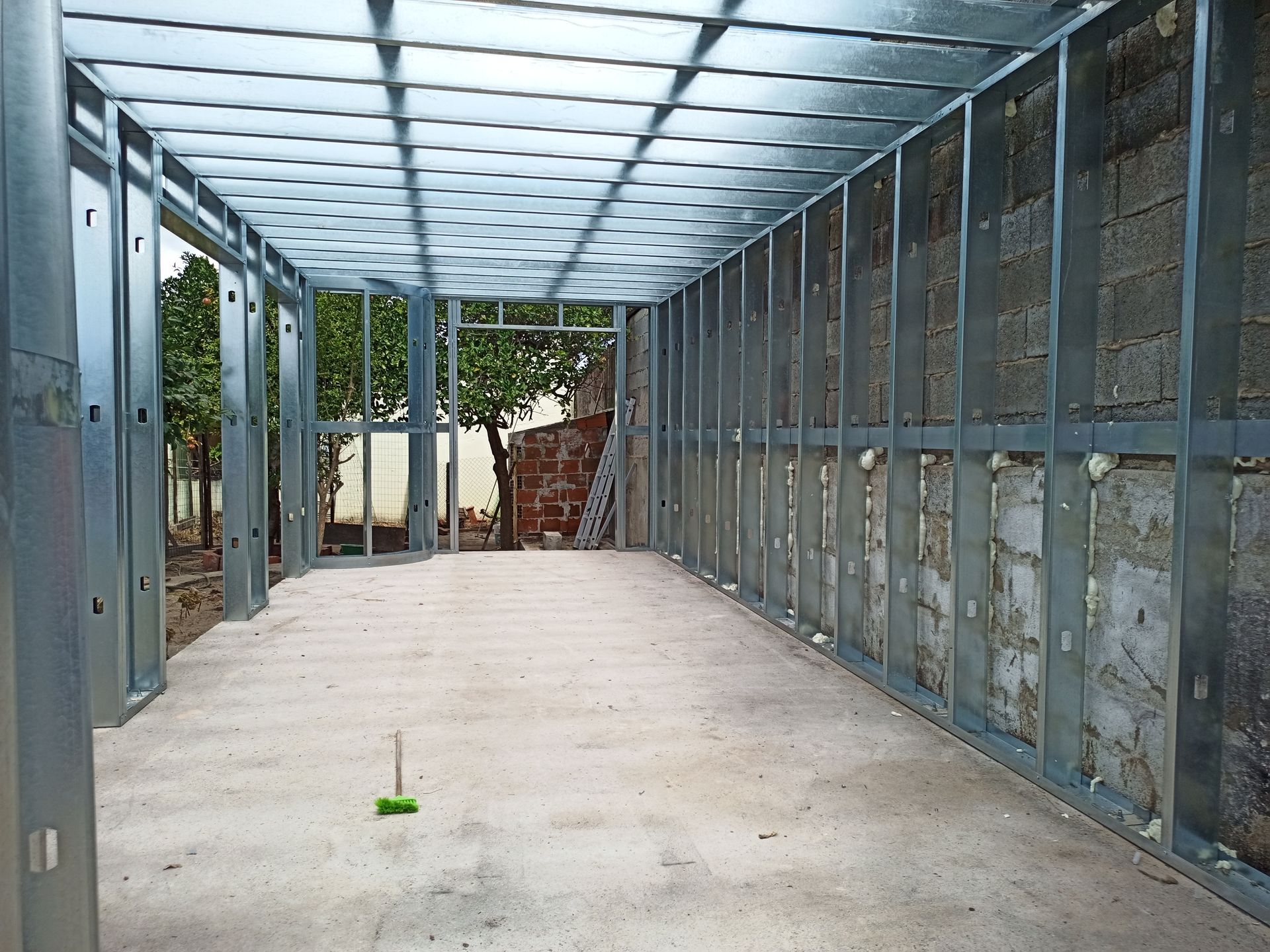 Vista interior de uma sala em construção com estrutura metálica para paredes e teto, sobre um piso de concreto.