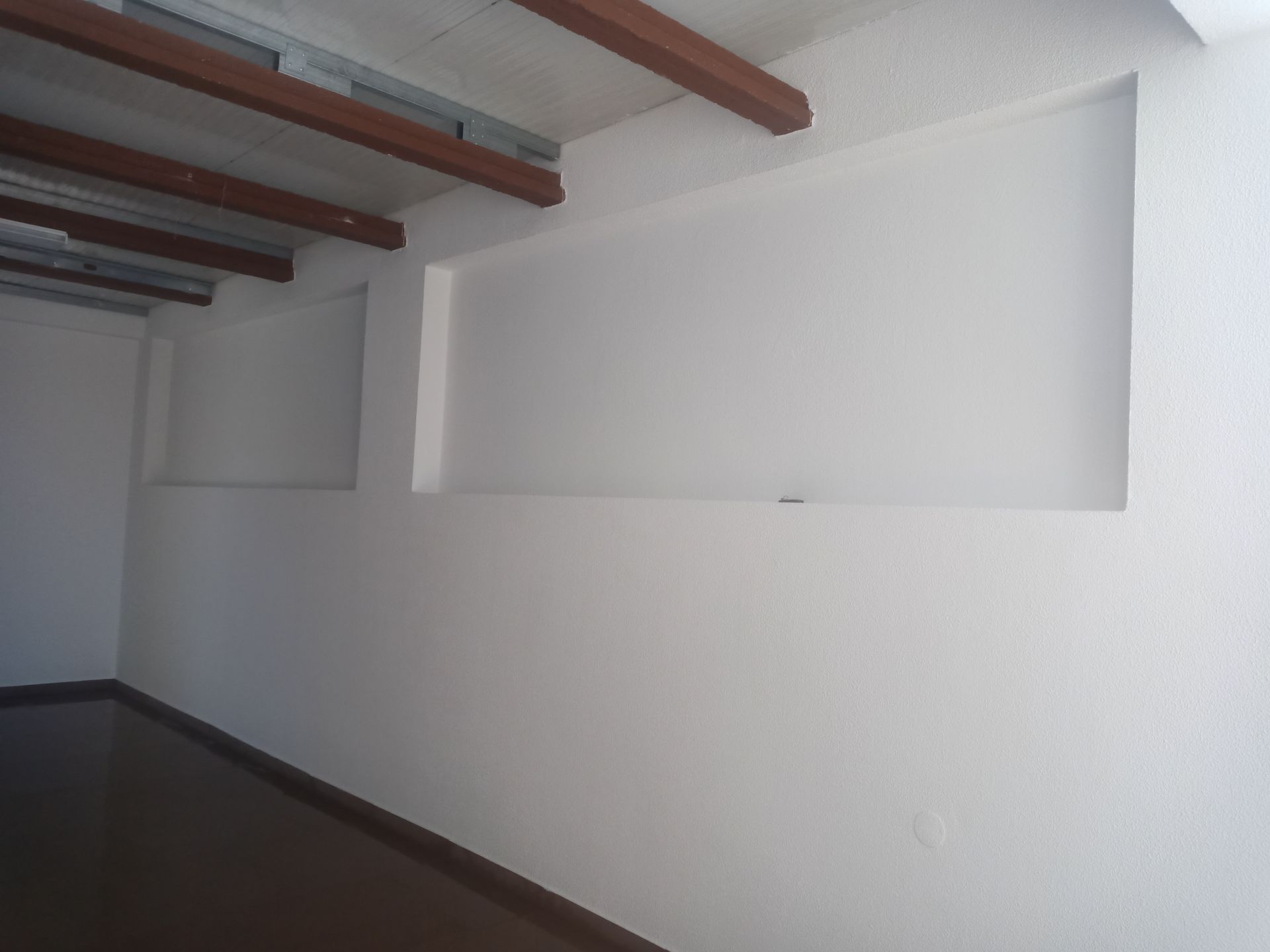 Sala branca e vazia com nichos embutidos nas paredes e vigas de madeira marrom no teto.