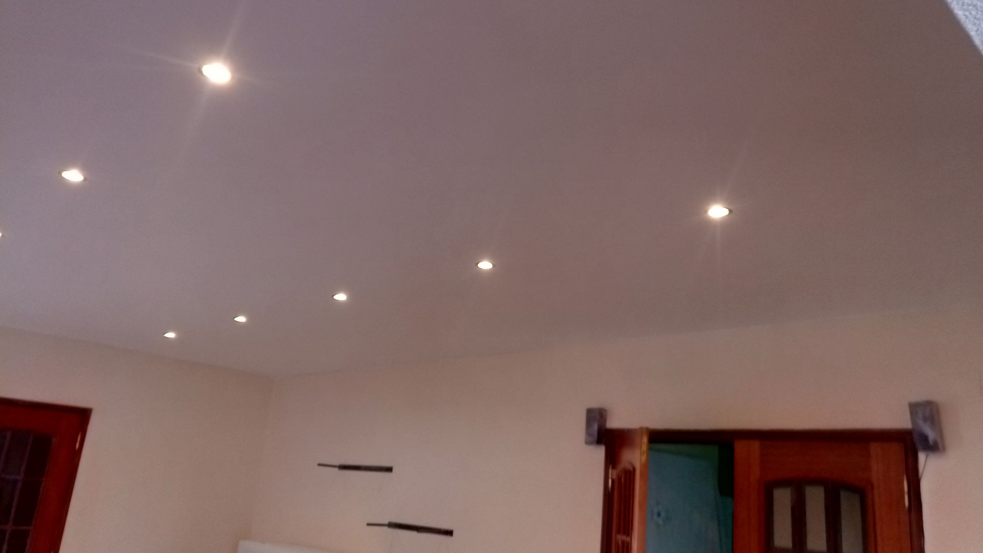 Teto branco com iluminação embutida. Paredes em tom creme, portas e janelas com caixilhos de madeira.