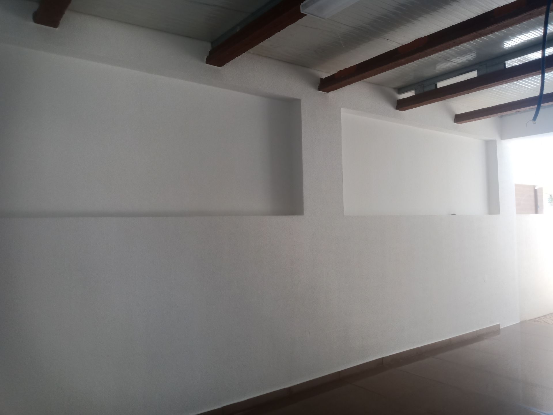 Quarto interior branco com seções de parede embutidas e vigas de madeira expostas no teto.