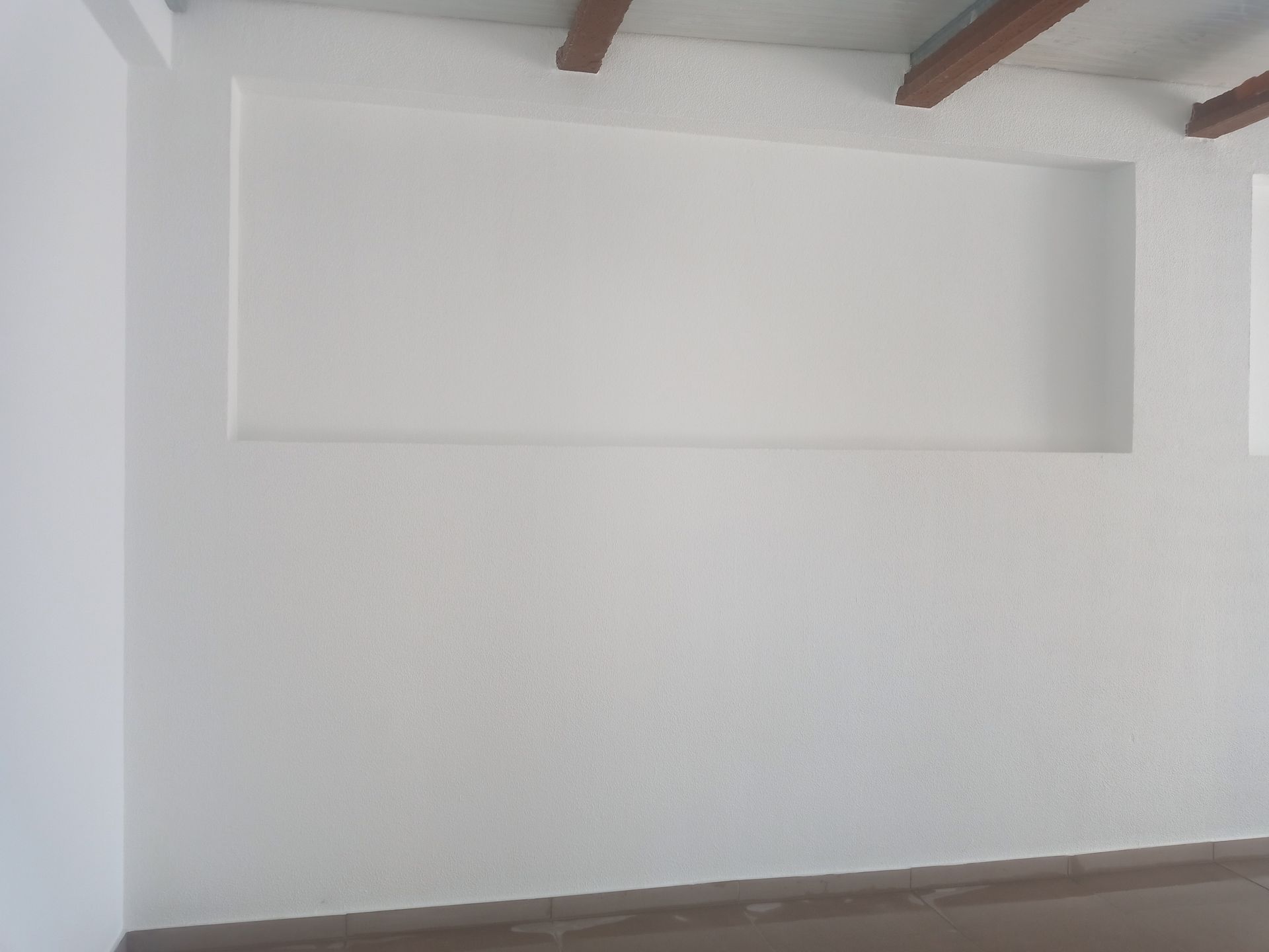 Parede branca com um retângulo embutido e vigas de madeira acima.