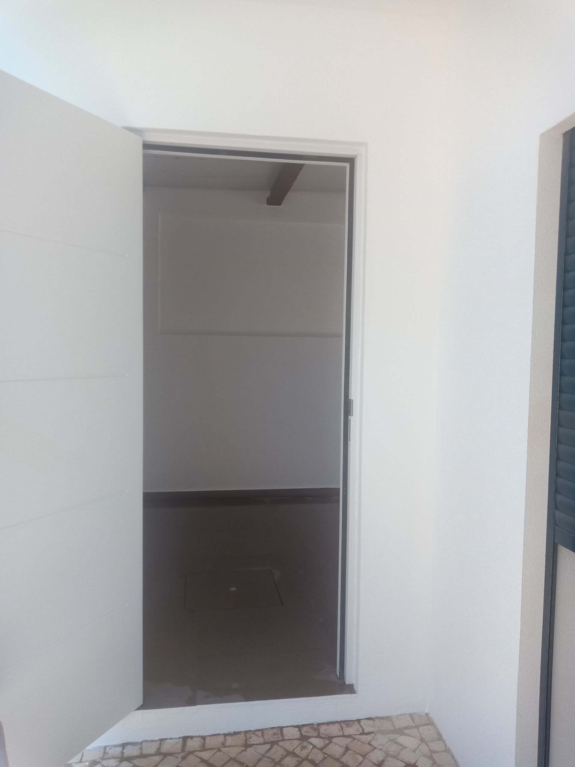 Abrir uma porta branca dá acesso a um pequeno espaço interior escuro, com paredes brancas e uma parte inferior escura.