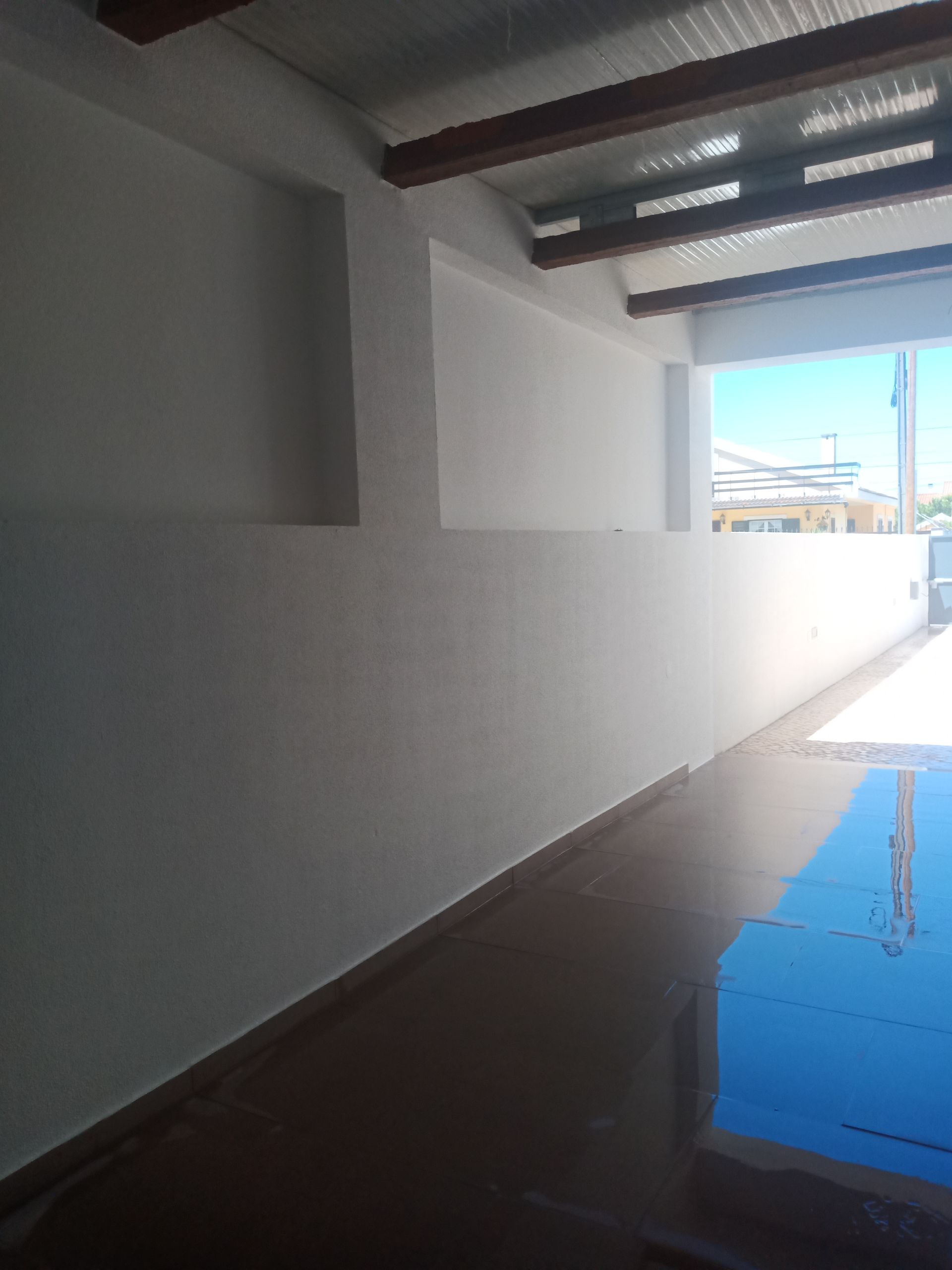 Espaço interior com paredes brancas, piso brilhante e reflexivo e uma porta aberta para o exterior.