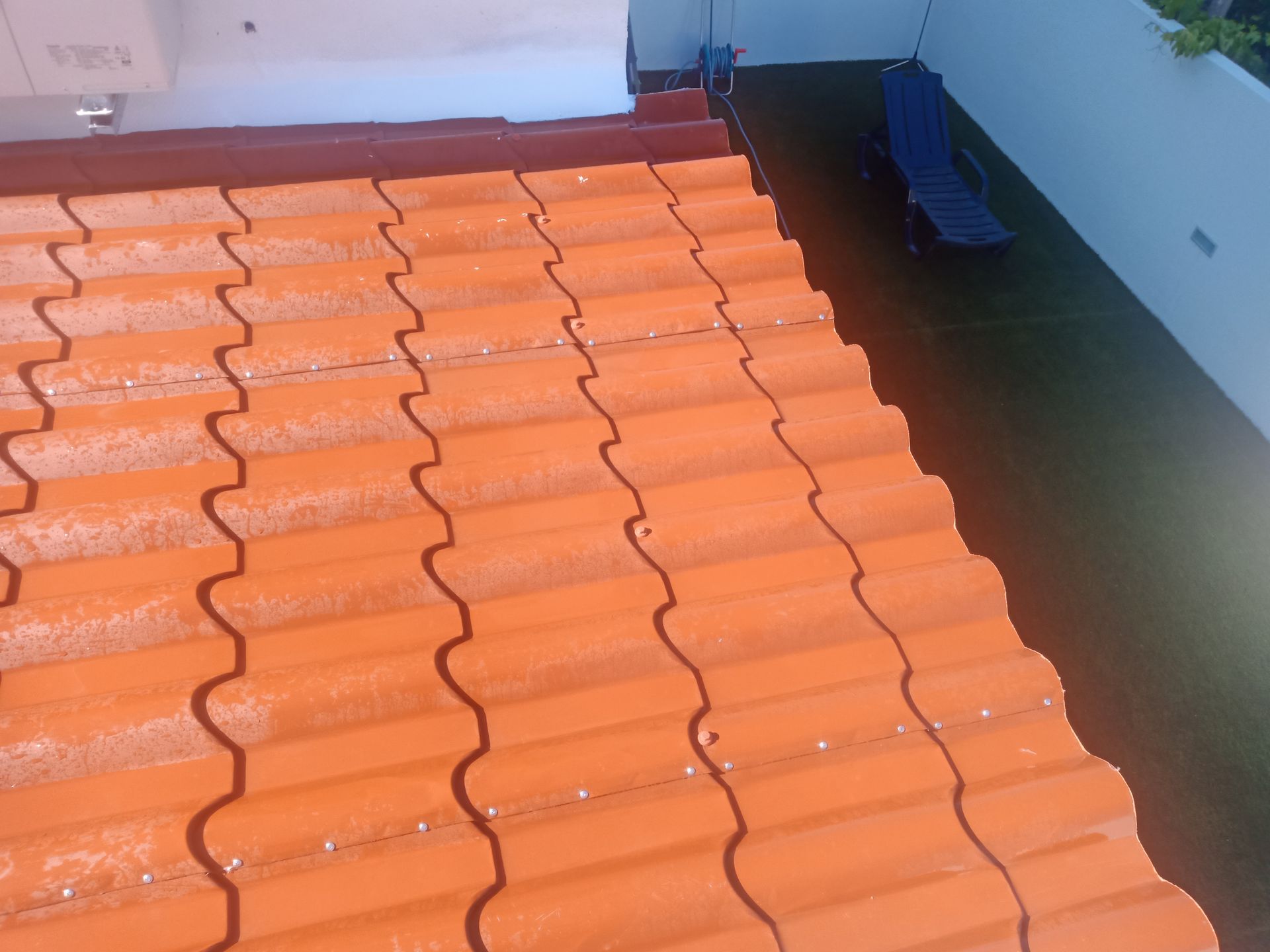 Telhado de telha laranja com parede branca e um escorregador azul ao fundo.