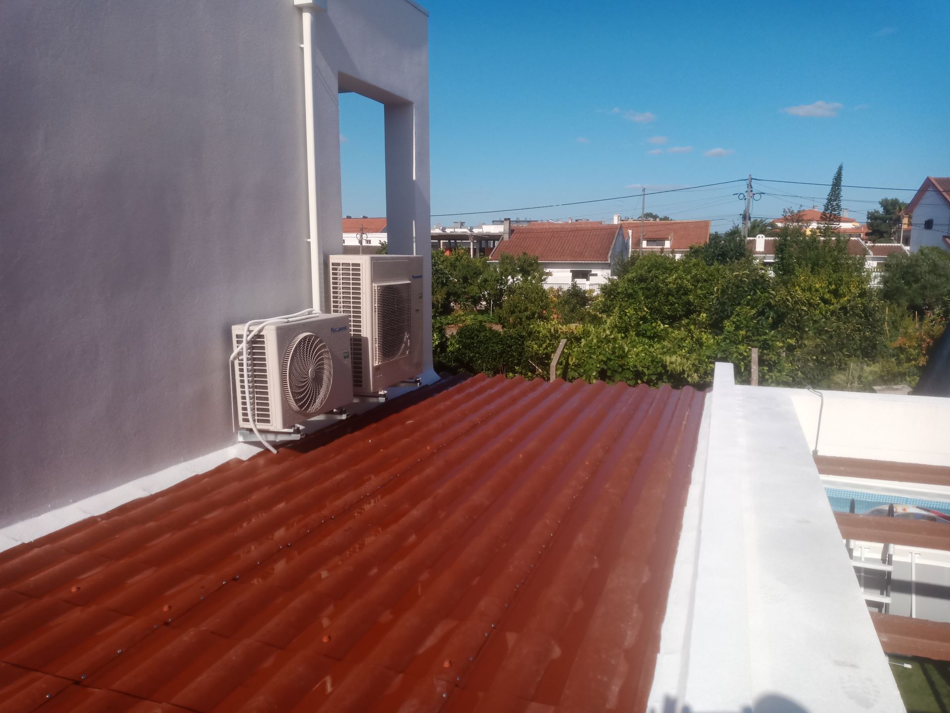 Telhado de zinco vermelho com unidades de ar condicionado e vista para casas e árvores.