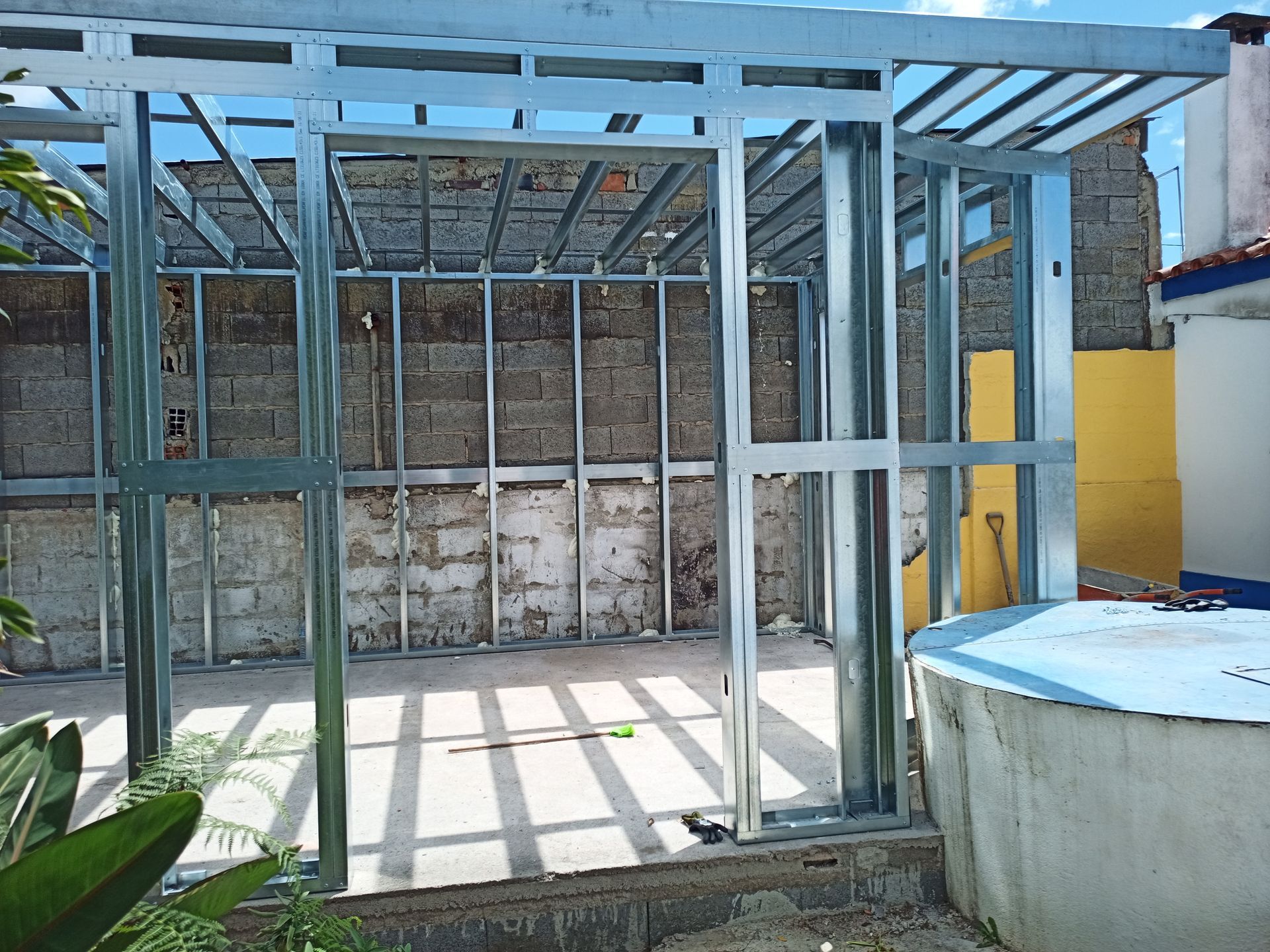 Estrutura de aço sendo construída contra uma parede de tijolos, com a luz do sol projetando sombras.