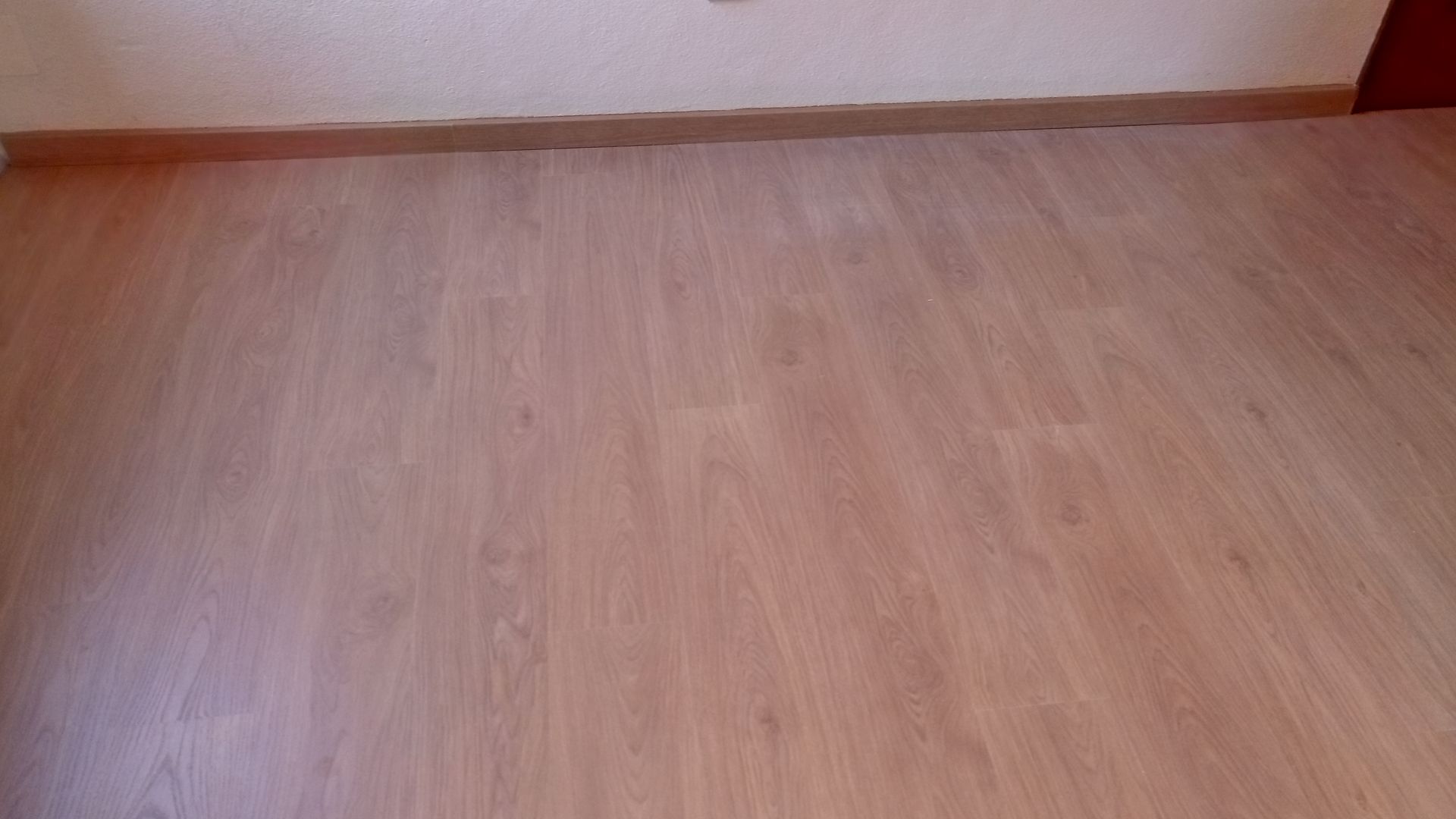 Piso de madeira marrom claro com rodapé marrom claro contra uma parede branca.