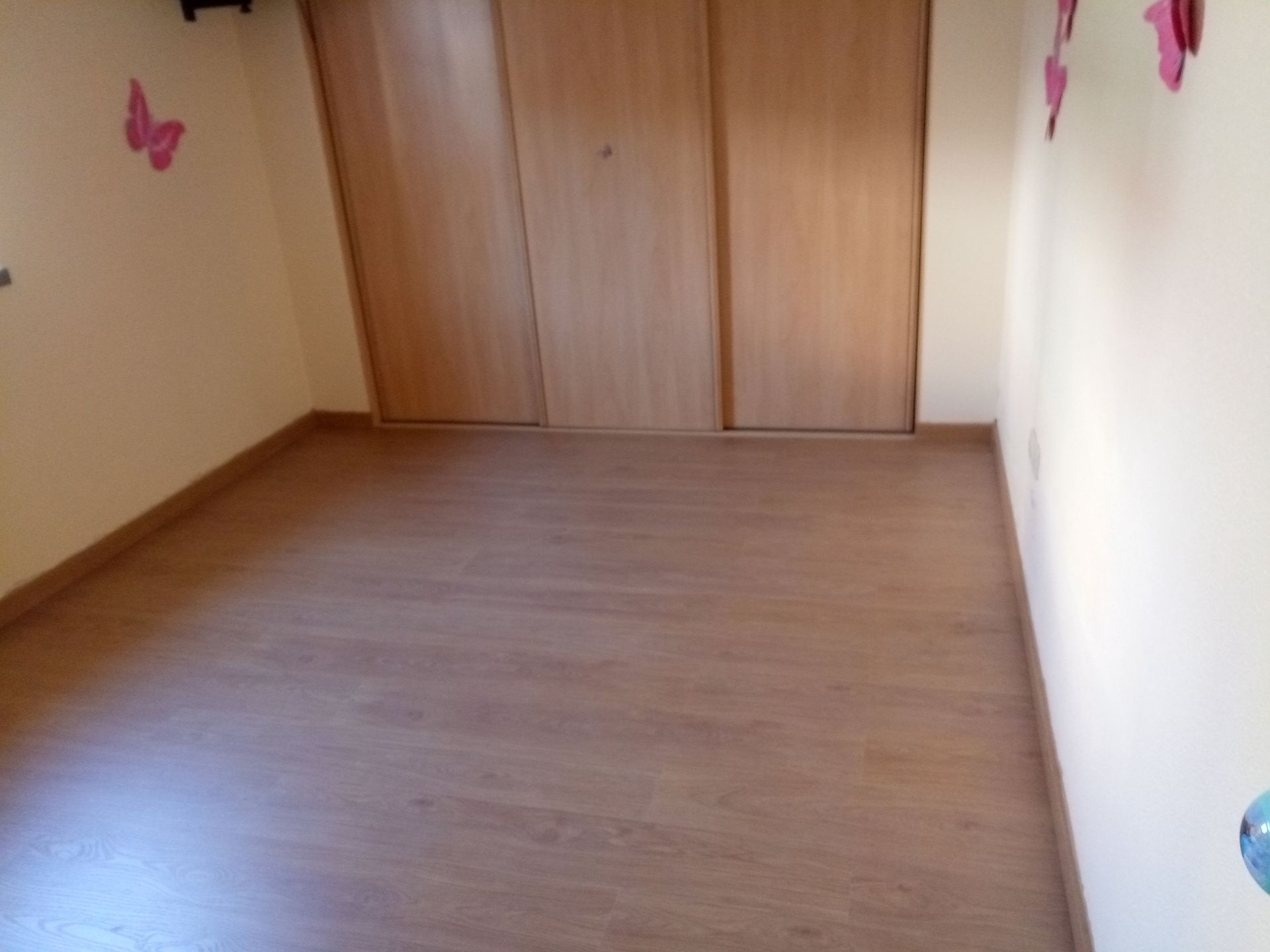 Quarto vazio com piso imitando madeira e um armário de três portas; as paredes são pintadas de bege claro.