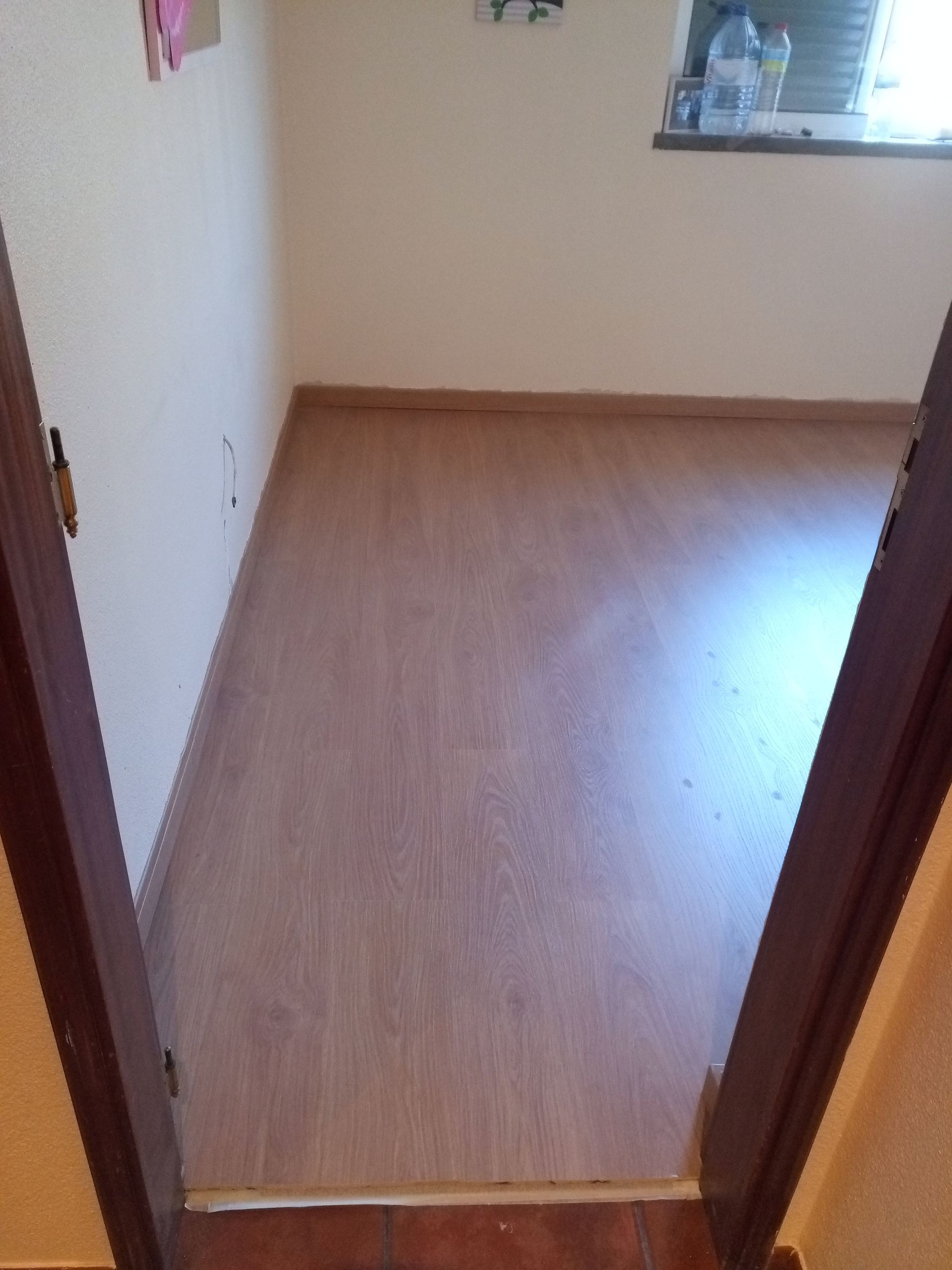 Vista para um pequeno quarto com piso que imita madeira e uma janela.