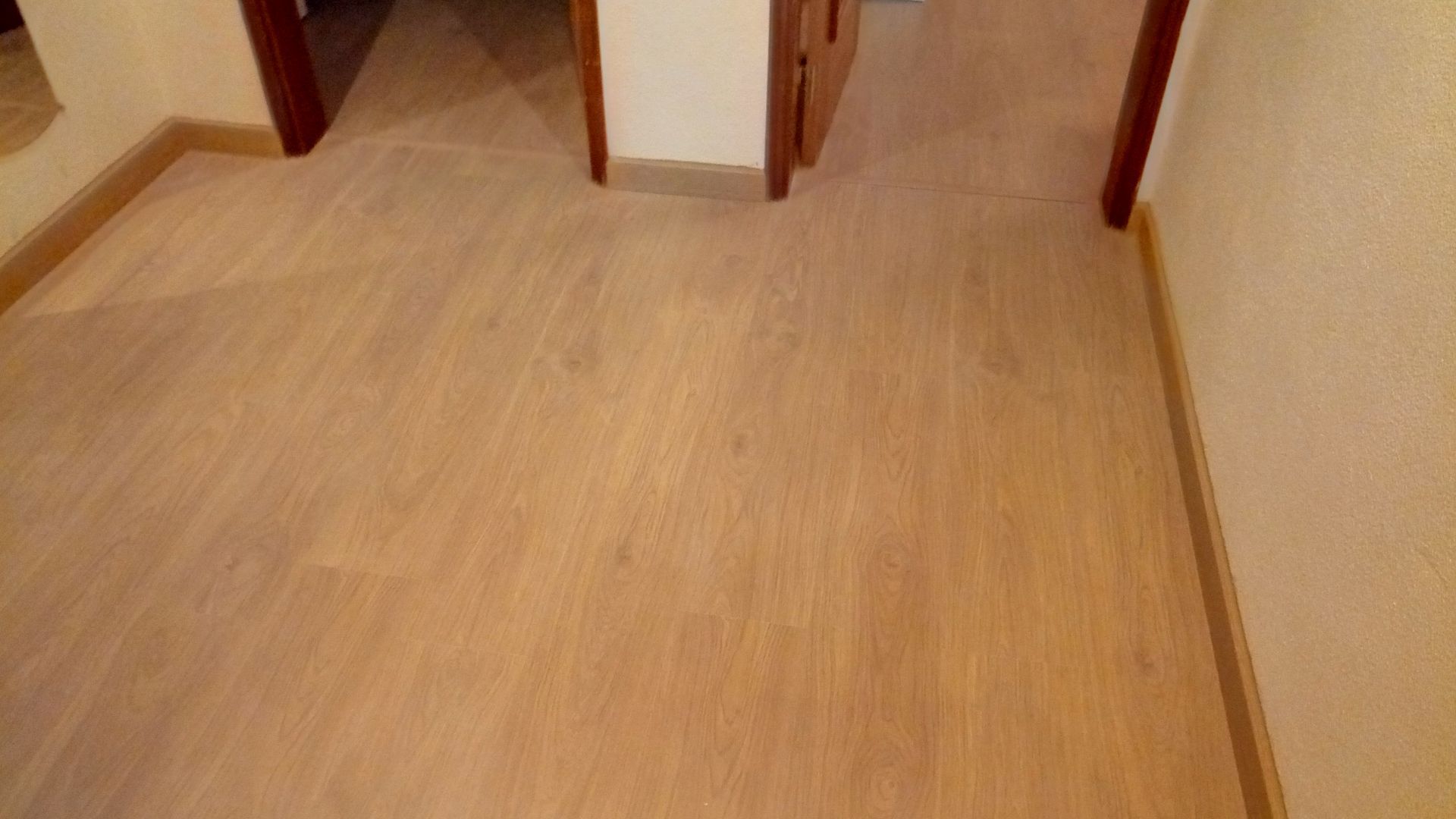 Piso de madeira clara em um corredor com portas em ambos os lados.