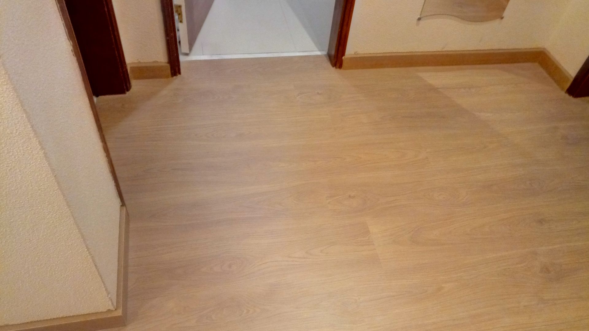 Piso de madeira clara em um corredor com portas em ambos os lados e uma parede de cor clara.