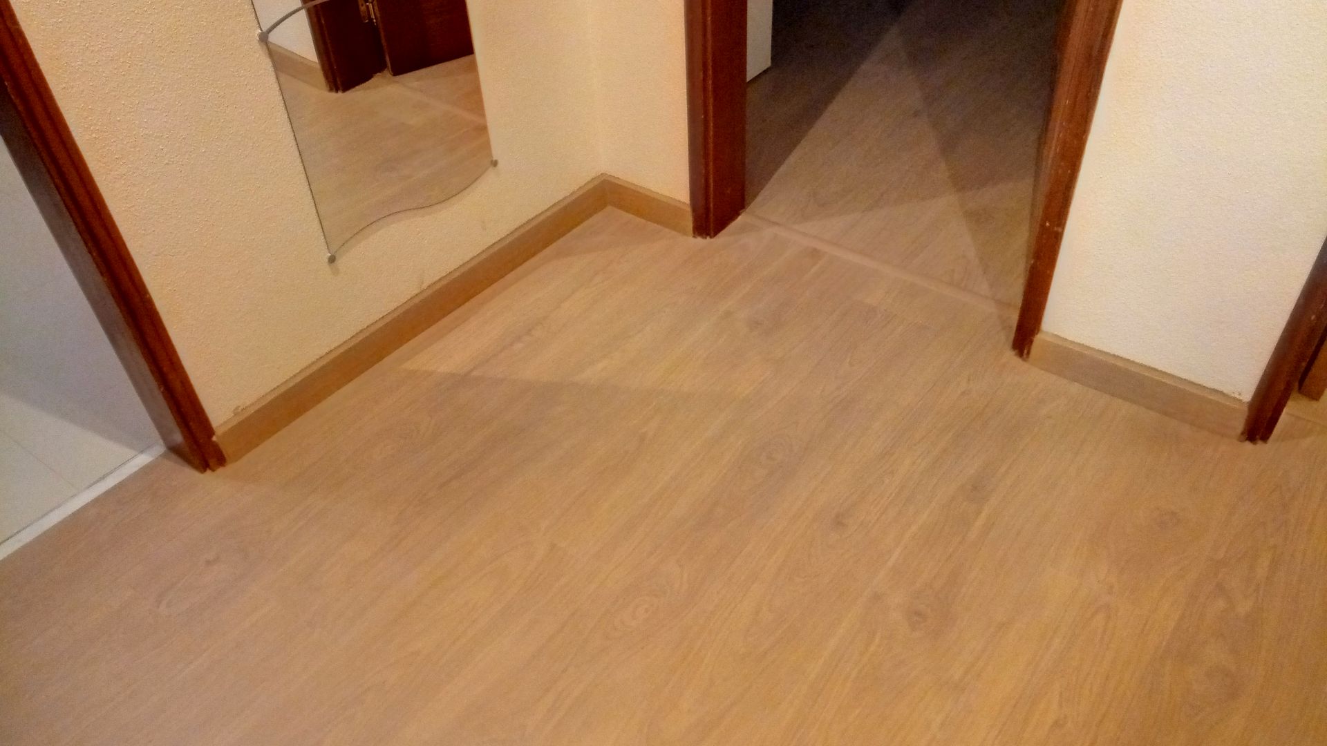 Corredor com piso de madeira, batentes de porta marrons e paredes bege.