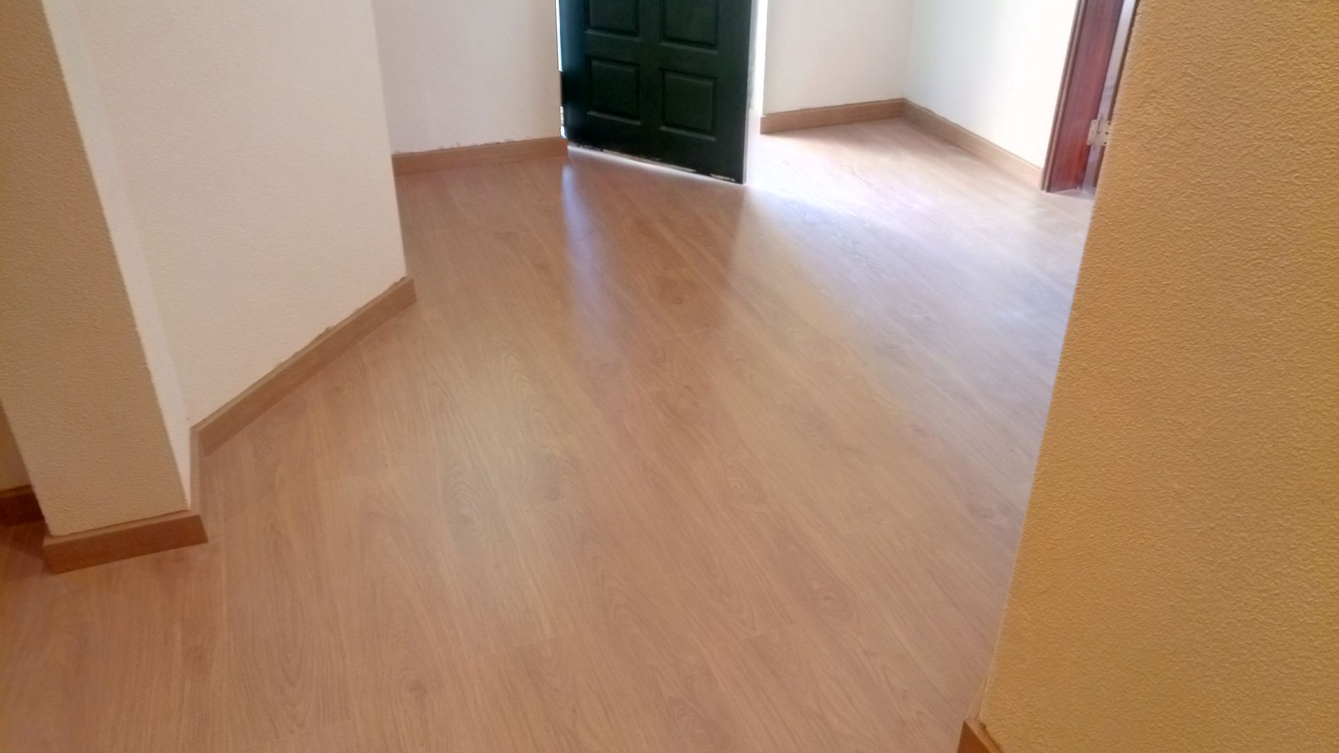 Piso de madeira em um quarto com paredes cor creme e porta verde-escura.