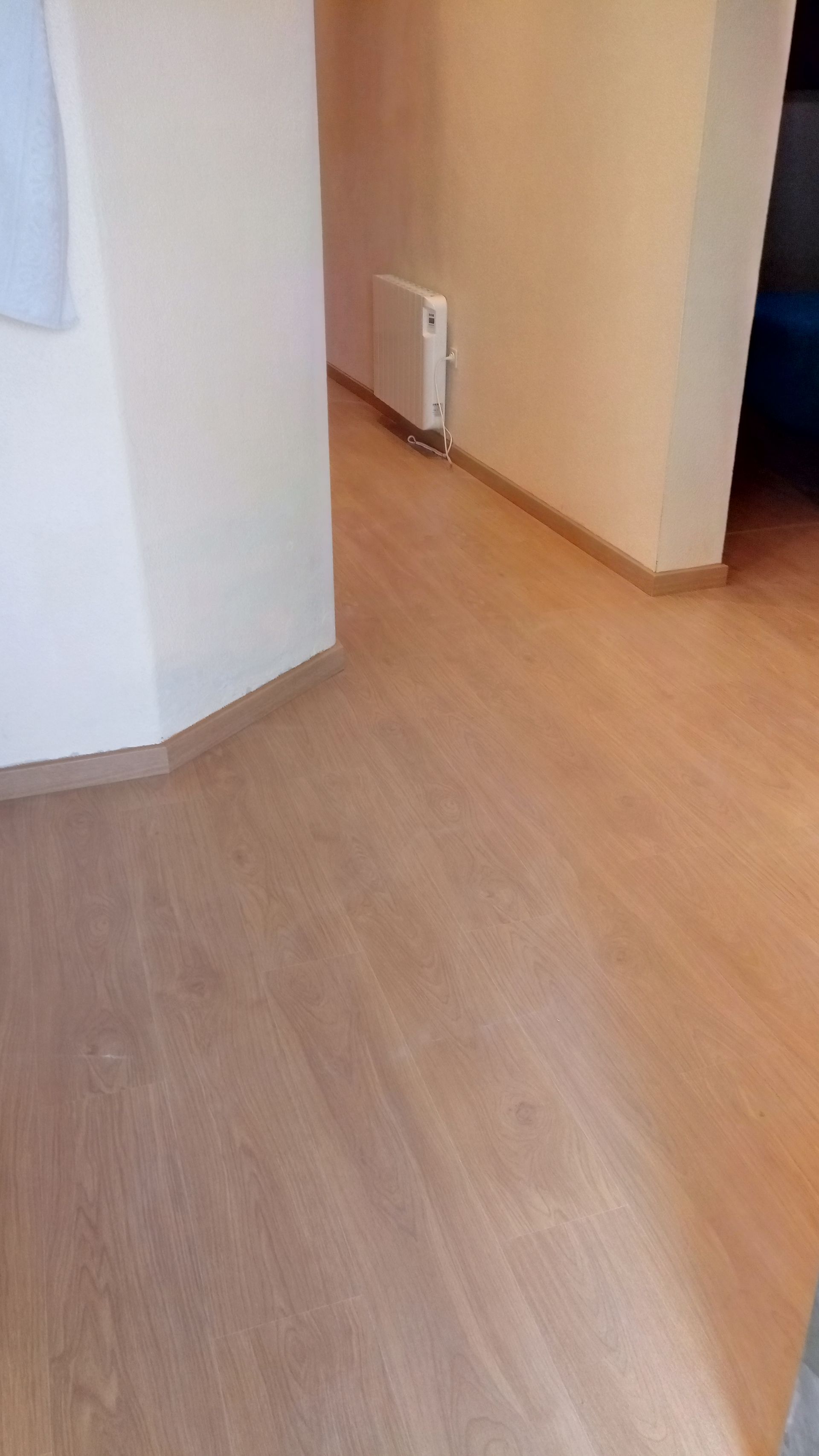 Corredor com piso de madeira, paredes brancas e um radiador.
