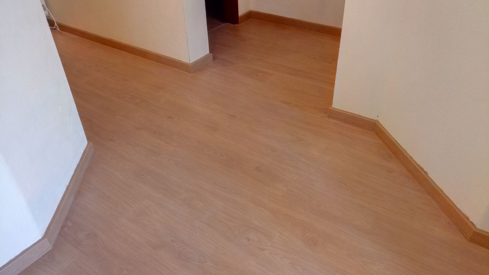 Corredor com piso laminado marrom claro e paredes brancas.