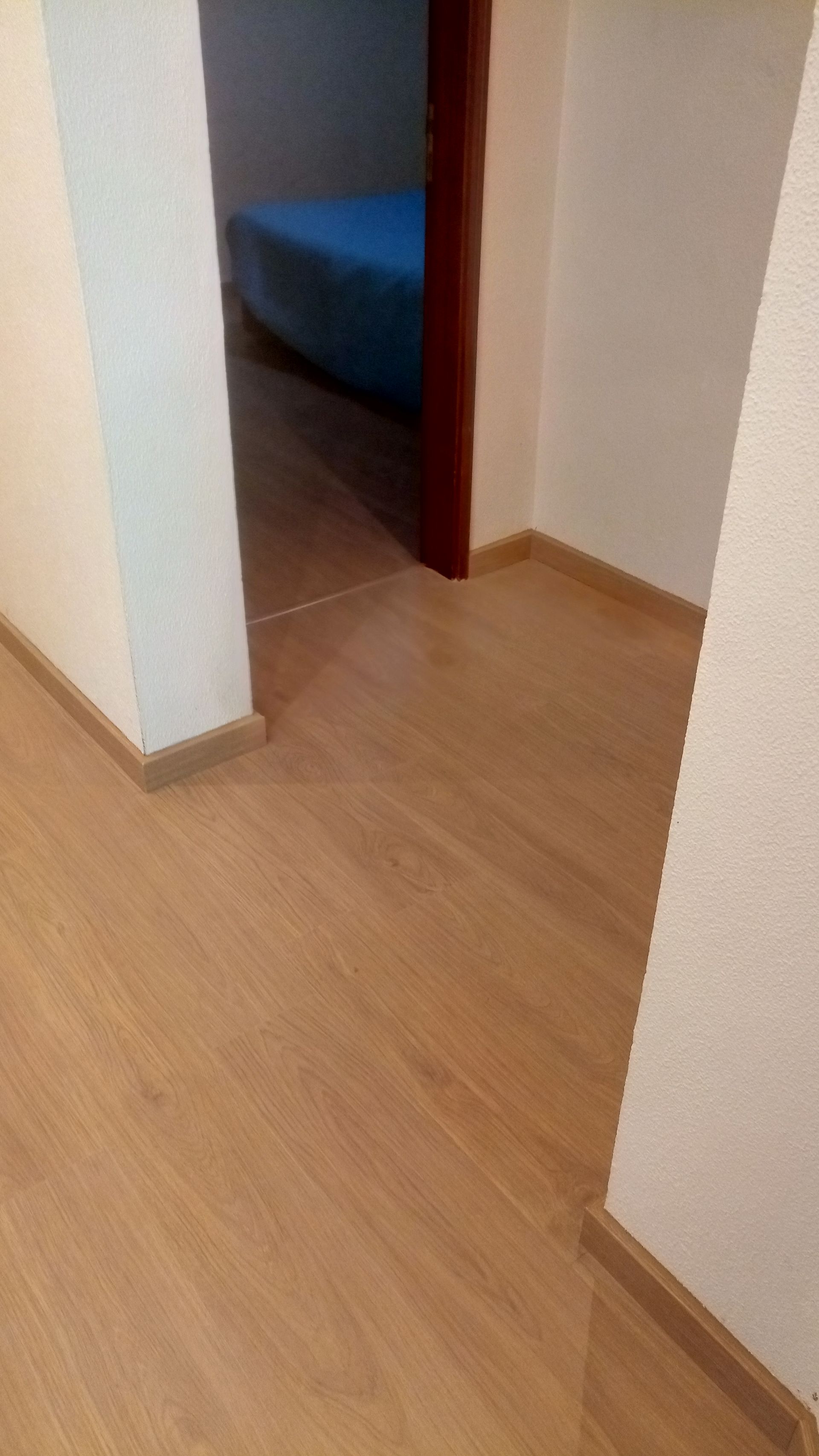 Piso de madeira com rodapés que leva a uma porta, com vista para o quarto e um colchão azul.